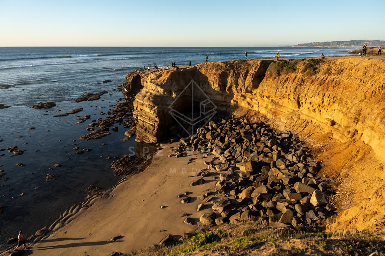 Elevated view of the cliffs, the surf and the ocean at Sunset Cliffs, with people walking.