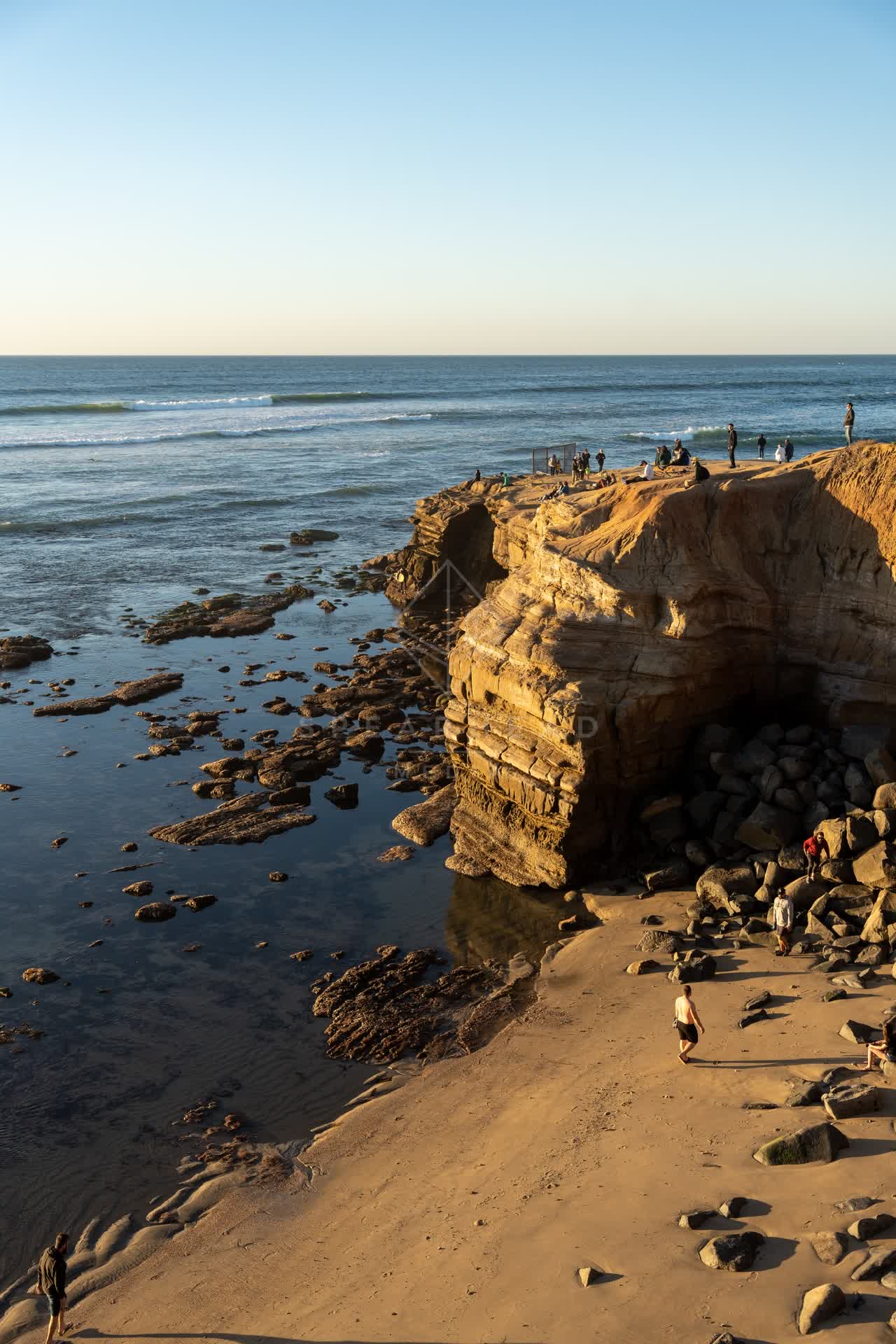 Elevated view of the cliffs, the surf and the ocean at Sunset Cliffs, with people walking.