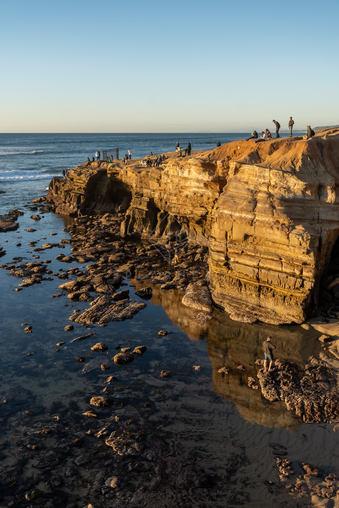 Elevated view of the cliffs, the surf and the ocean at Sunset Cliffs, with people walking.