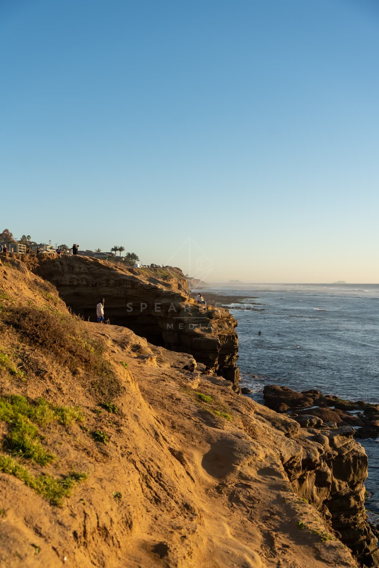 Elevated view of the cliffs, palm trees and the ocean at Sunset Cliffs, with people walking.