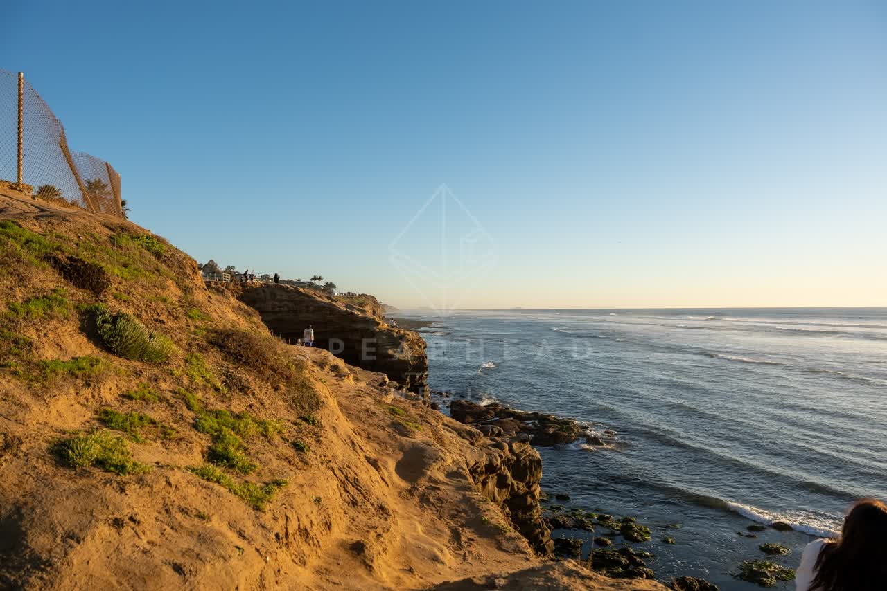 Elevated view of the cliffs, the surf and the ocean at Sunset Cliffs, with people walking.