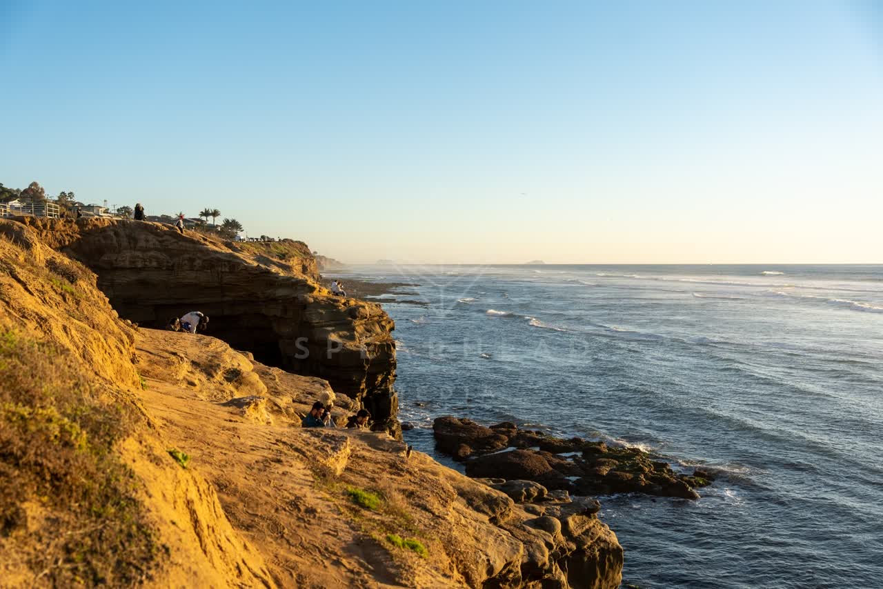Elevated view of the cliffs, the surf and the ocean at Sunset Cliffs, with a crowd gathered.