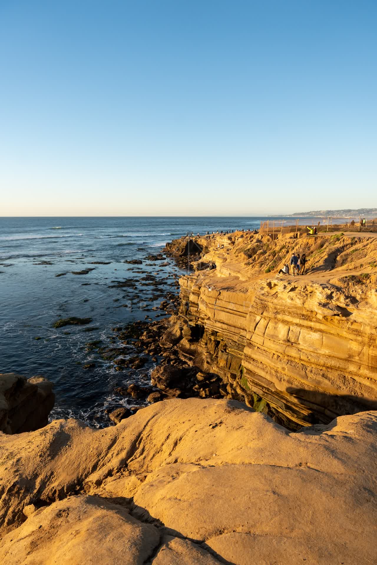Elevated view of the cliffs, the ocean and open country at Sunset Cliffs, with people walking.