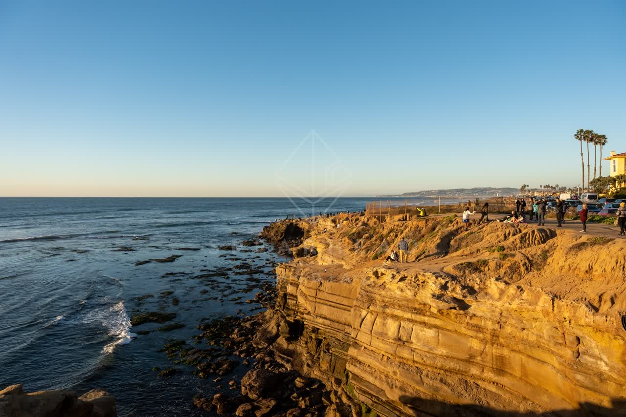 Elevated view of the cliffs, palm trees and the ocean at Sunset Cliffs, with a crowd gathered.