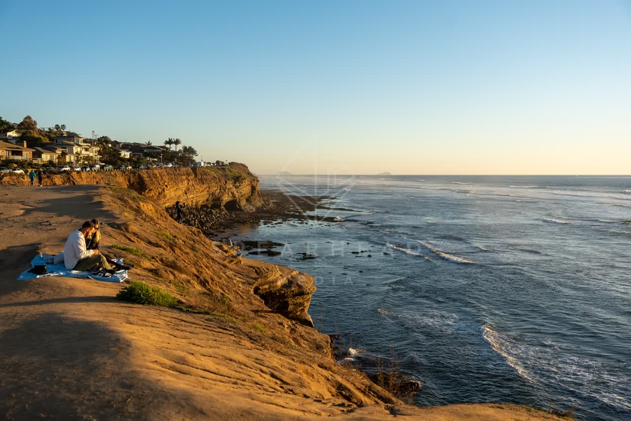 Elevated view of the cliffs, palm trees and the ocean at Sunset Cliffs, with a crowd gathered.