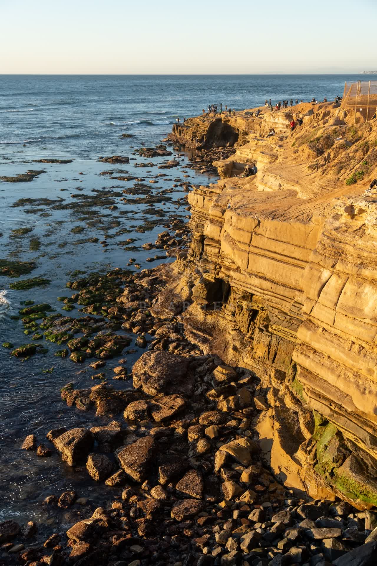 Elevated view of the cliffs, the ocean and open country at Sunset Cliffs, with people walking.
