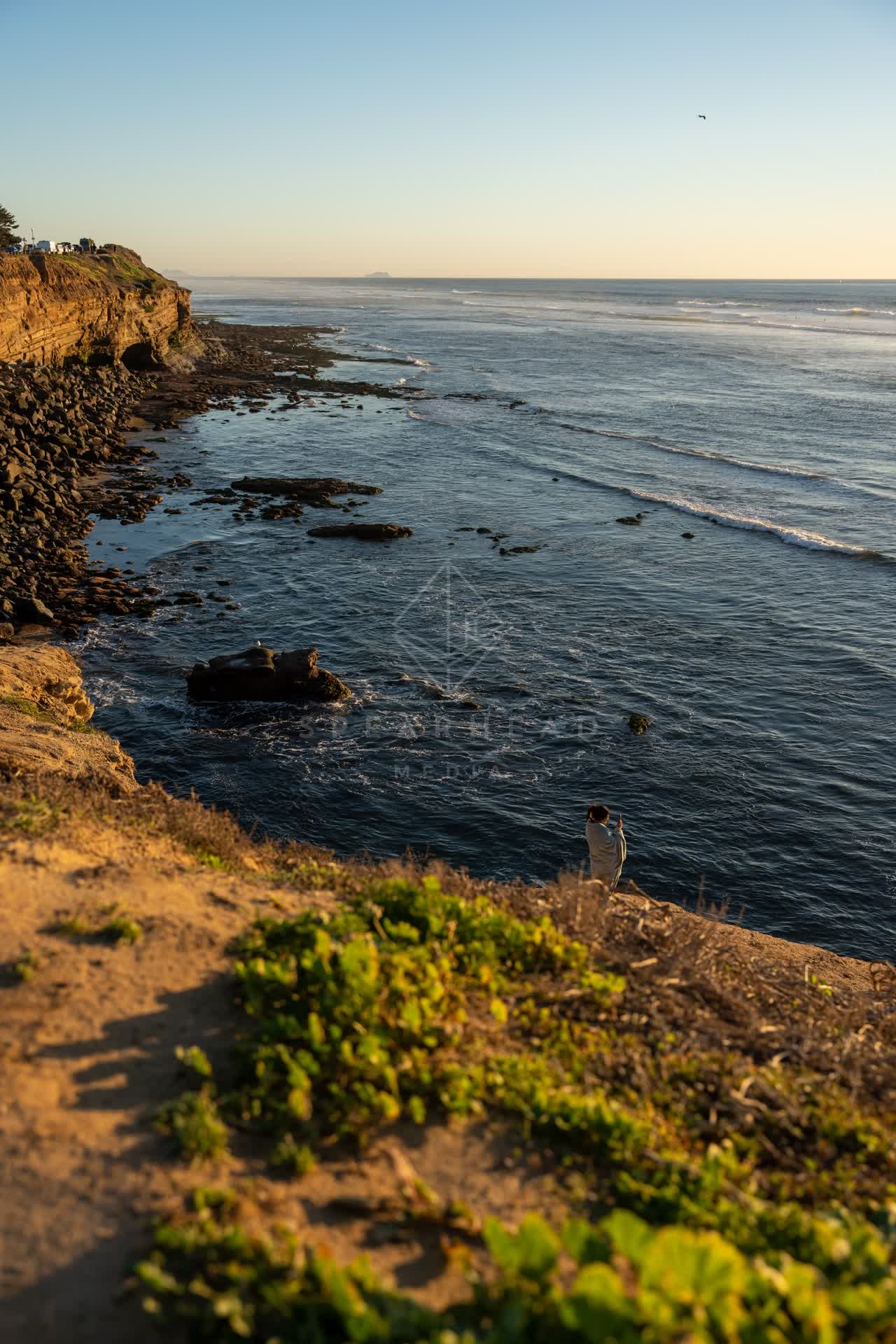 Elevated view of the cliffs, the surf and the ocean at Sunset Cliffs, with people walking.