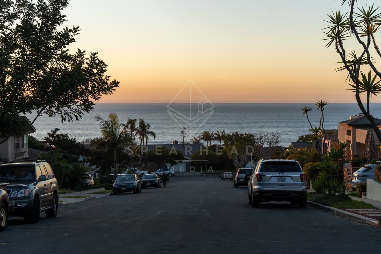 A residential street, palm trees and the ocean at Sunset Cliffs, with people walking.