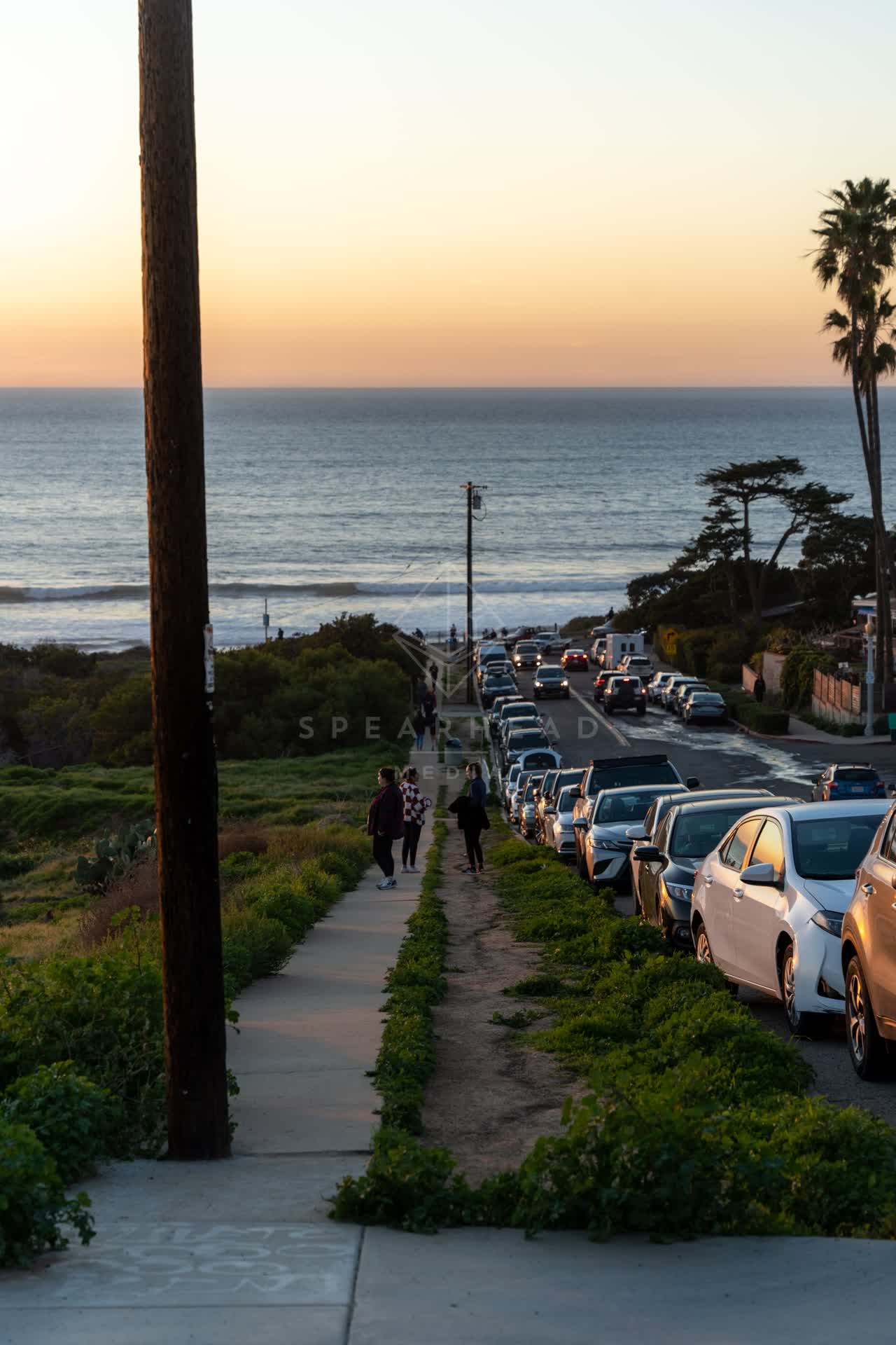 Elevated view of a residential street, the surf and palm trees at Sunset Cliffs, with people walking.