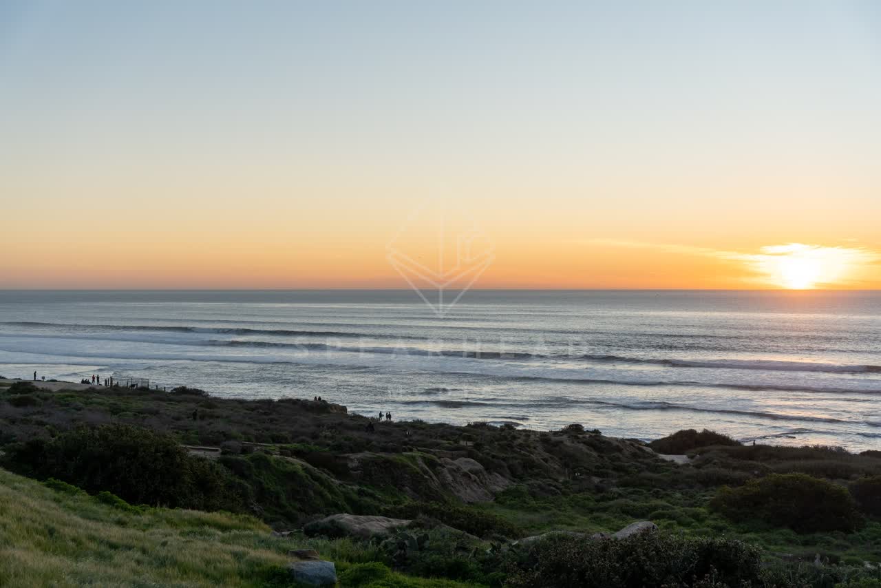 Elevated view of the cliffs, the surf and the ocean at Sunset Cliffs, with people walking.