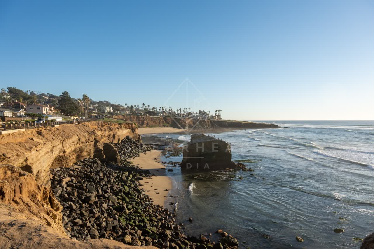 Elevated view of the cliffs, the surf and palm trees at Sunset Cliffs, with people walking.