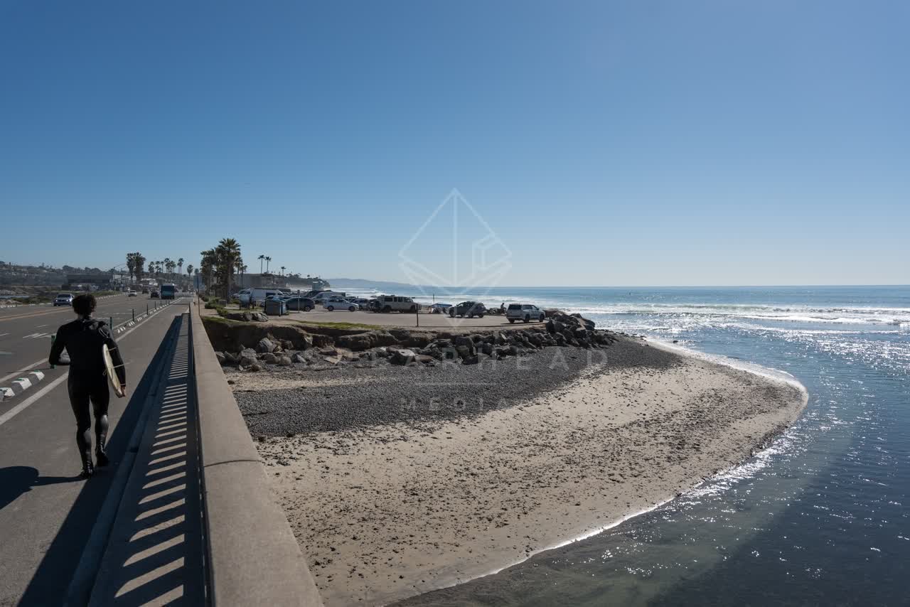 Elevated view of the beach, the surf and palm trees in Cardiff, with people walking.