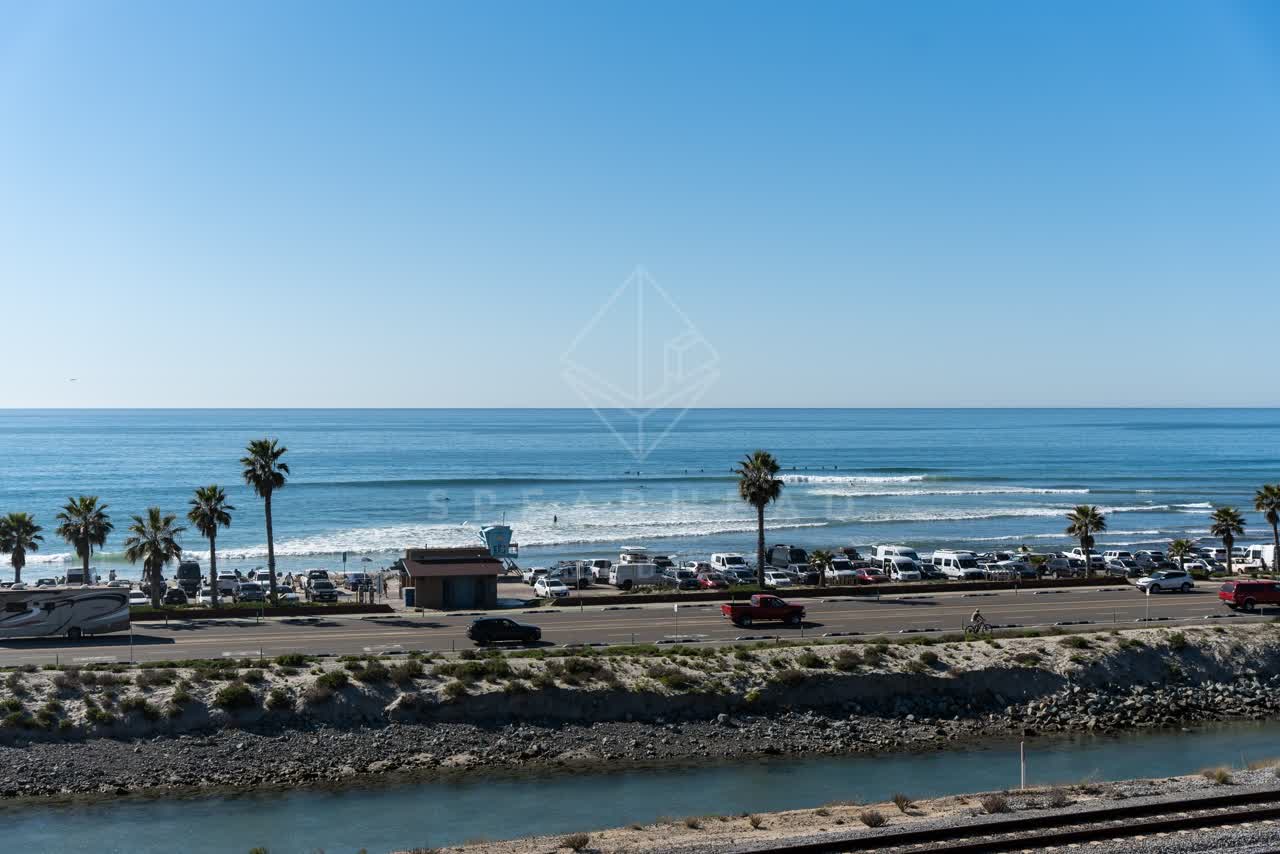 Elevated view of the beach, the surf and palm trees in Cardiff, with people walking.