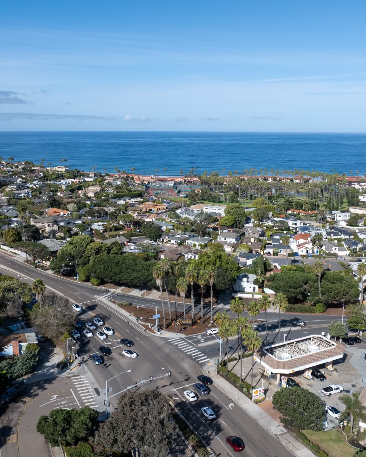 Aerial view of a residential street, palm trees and the ocean in La Jolla, with people walking.