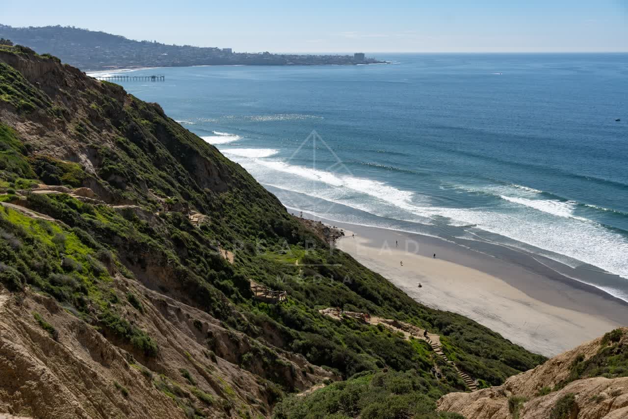 Elevated view of the cliffs, the surf and the pier at Torrey Pines, with people walking.