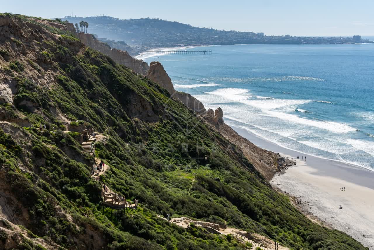 Elevated view of the cliffs, the surf and the pier at Torrey Pines, with people walking.