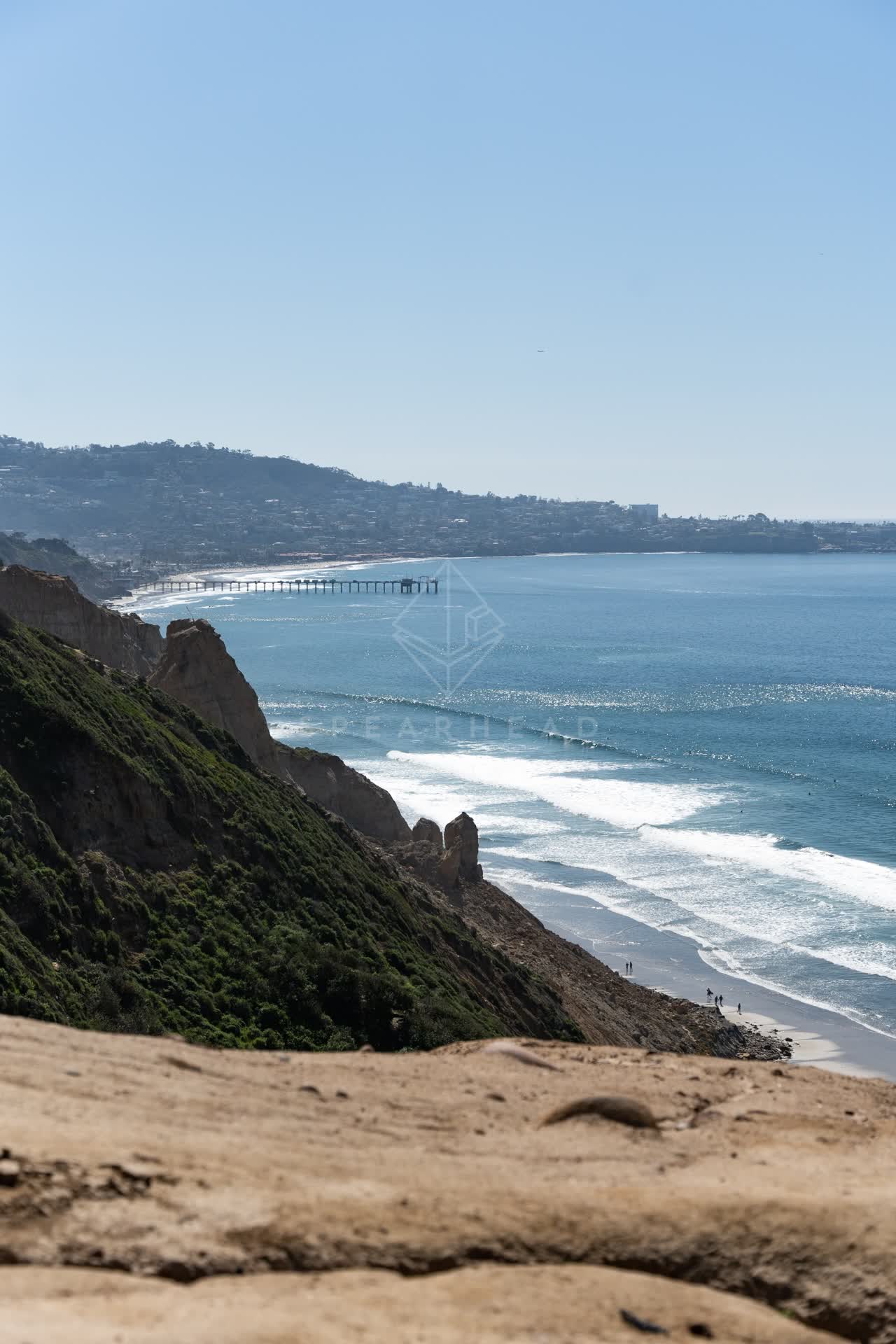Elevated view of the cliffs, the surf and the pier at Torrey Pines, with people walking.