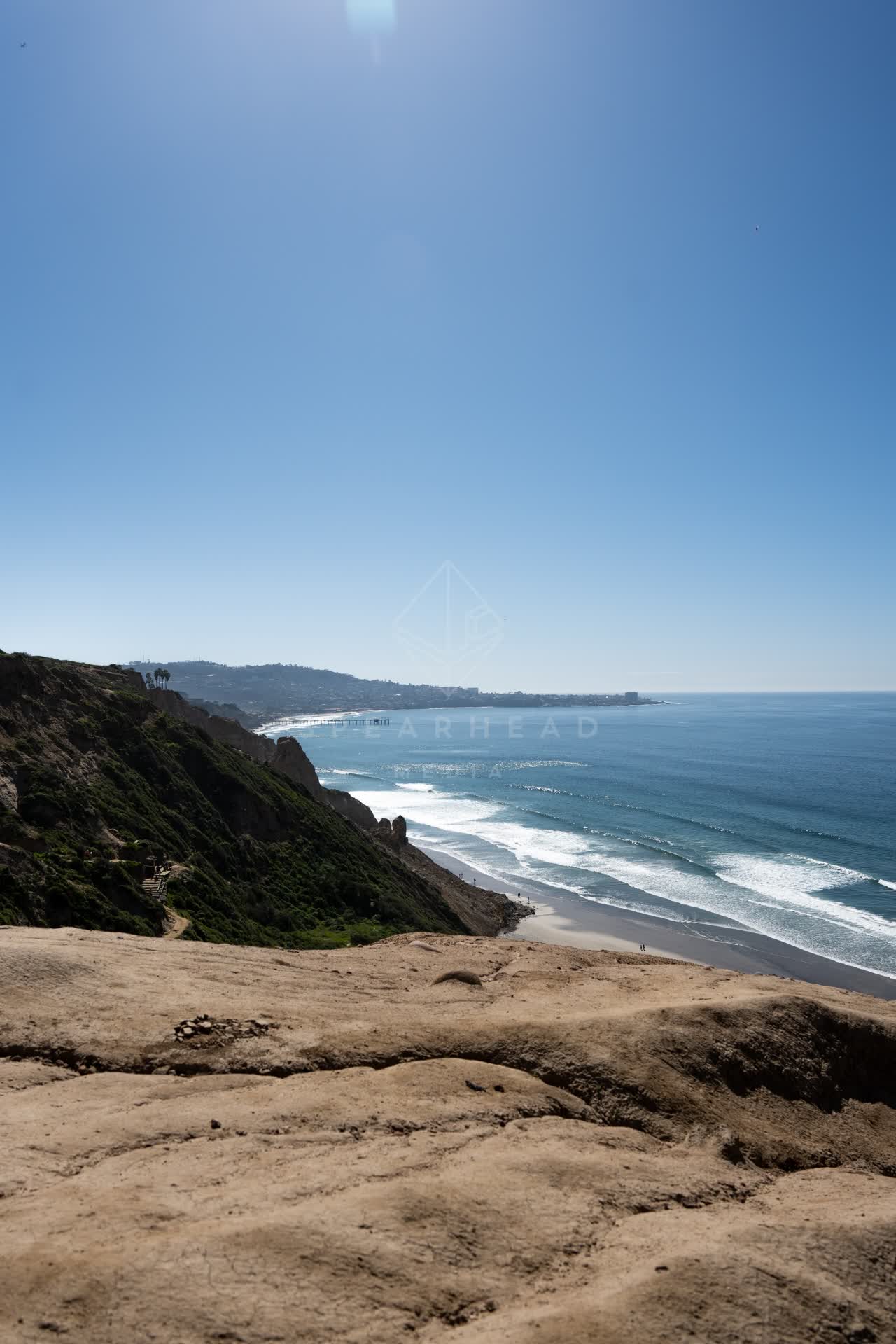 Elevated view of the cliffs, the surf and palm trees at Torrey Pines, with people walking.
