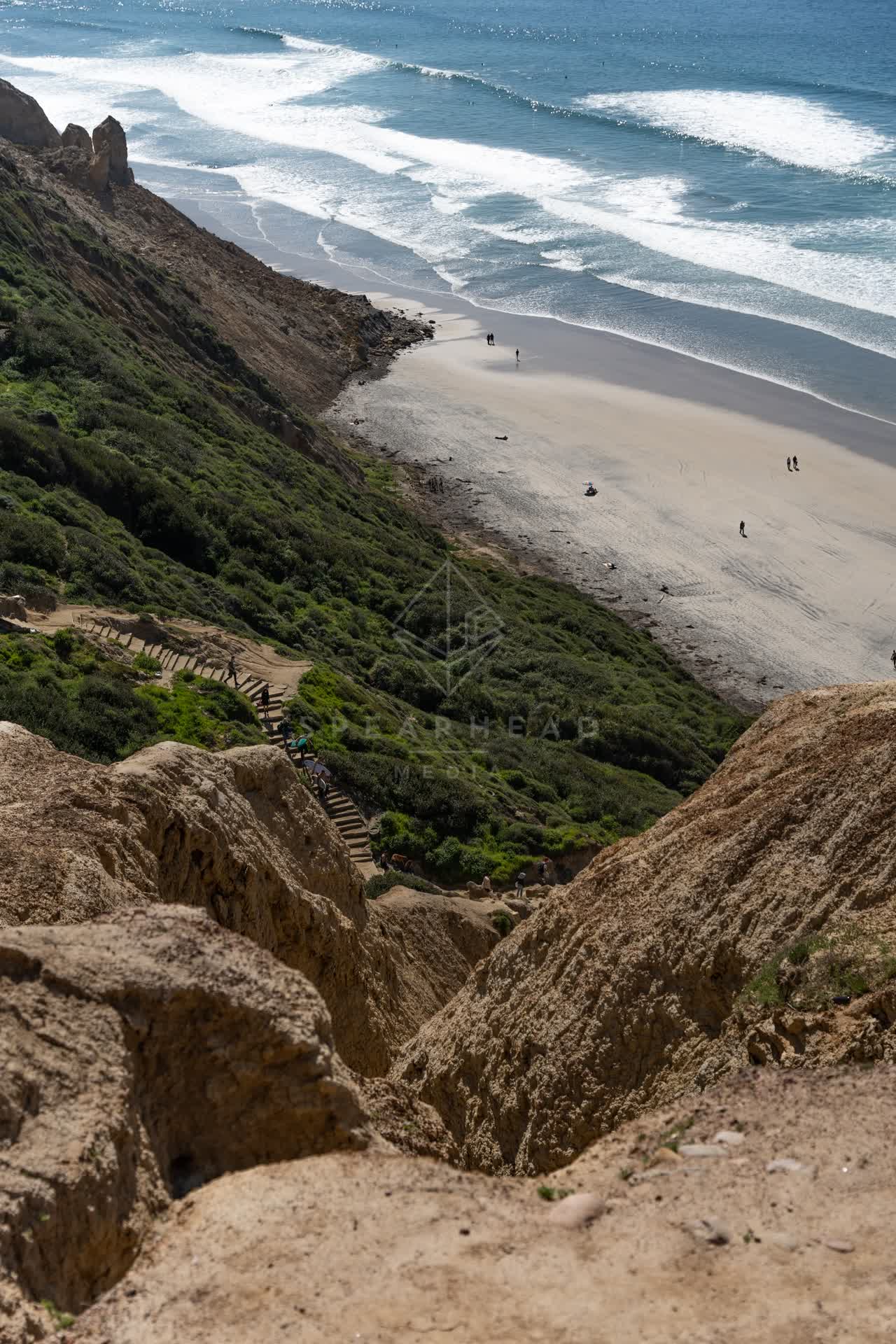 Elevated view of the cliffs, the surf and the ocean at Torrey Pines, with people walking.