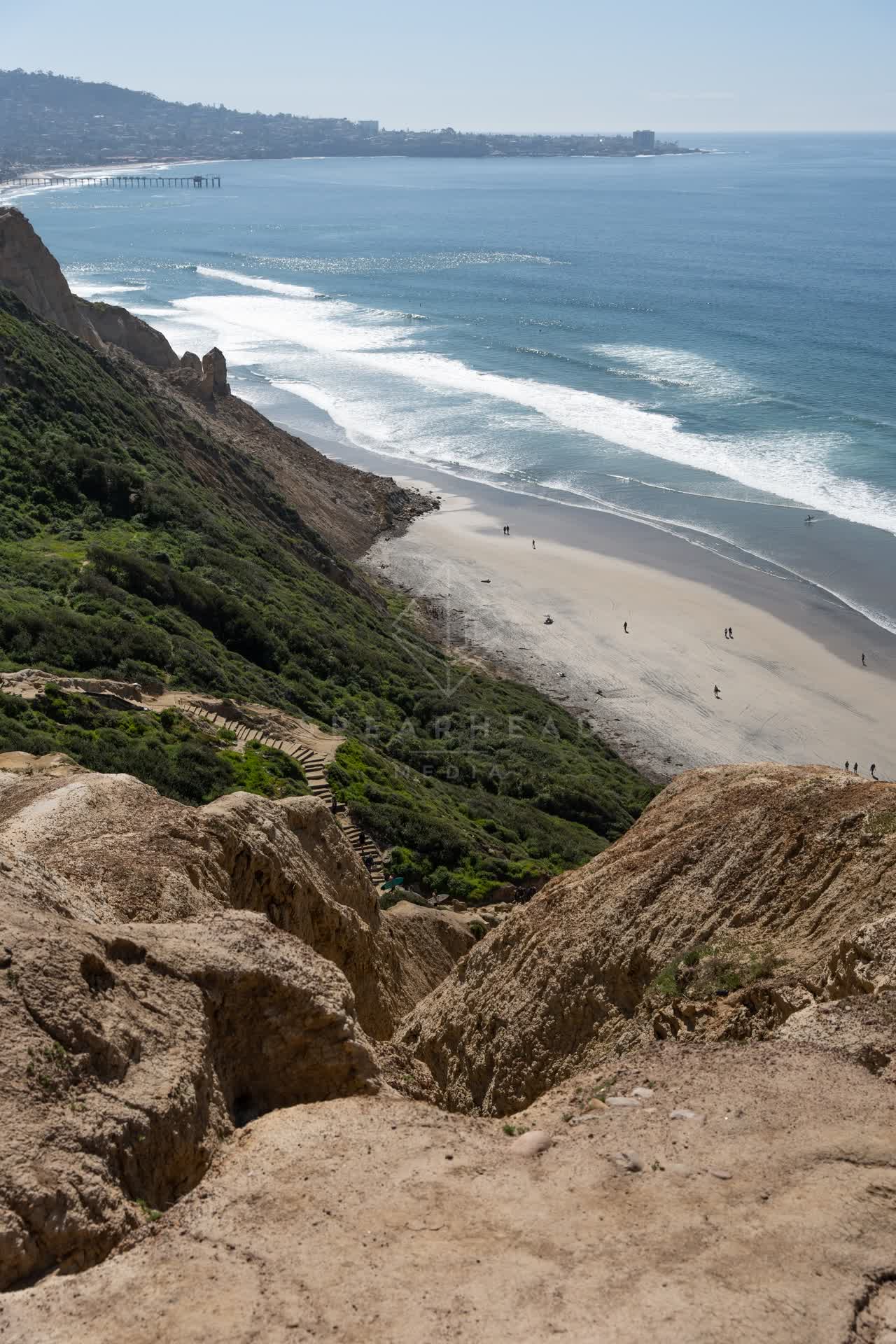 Elevated view of the cliffs, the surf and the pier at Torrey Pines, with people walking.