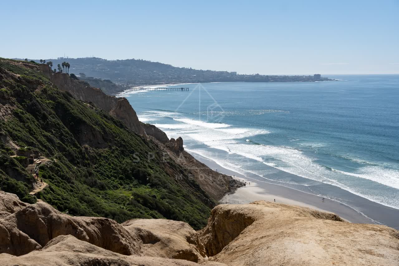 Elevated view of the cliffs, the surf and the pier at Torrey Pines, with people walking.