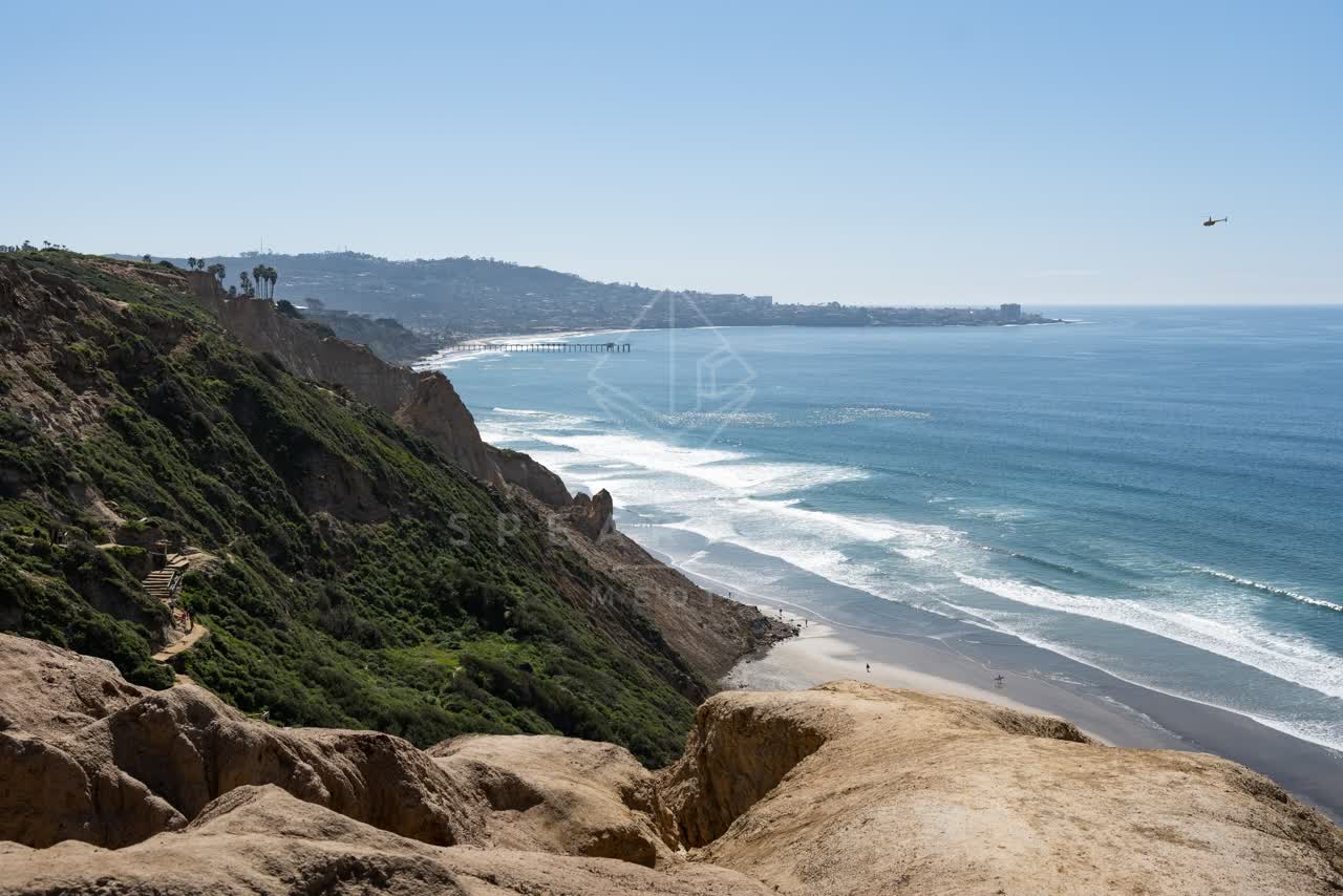 Elevated view of the cliffs, the surf and the pier at Torrey Pines, with people walking.
