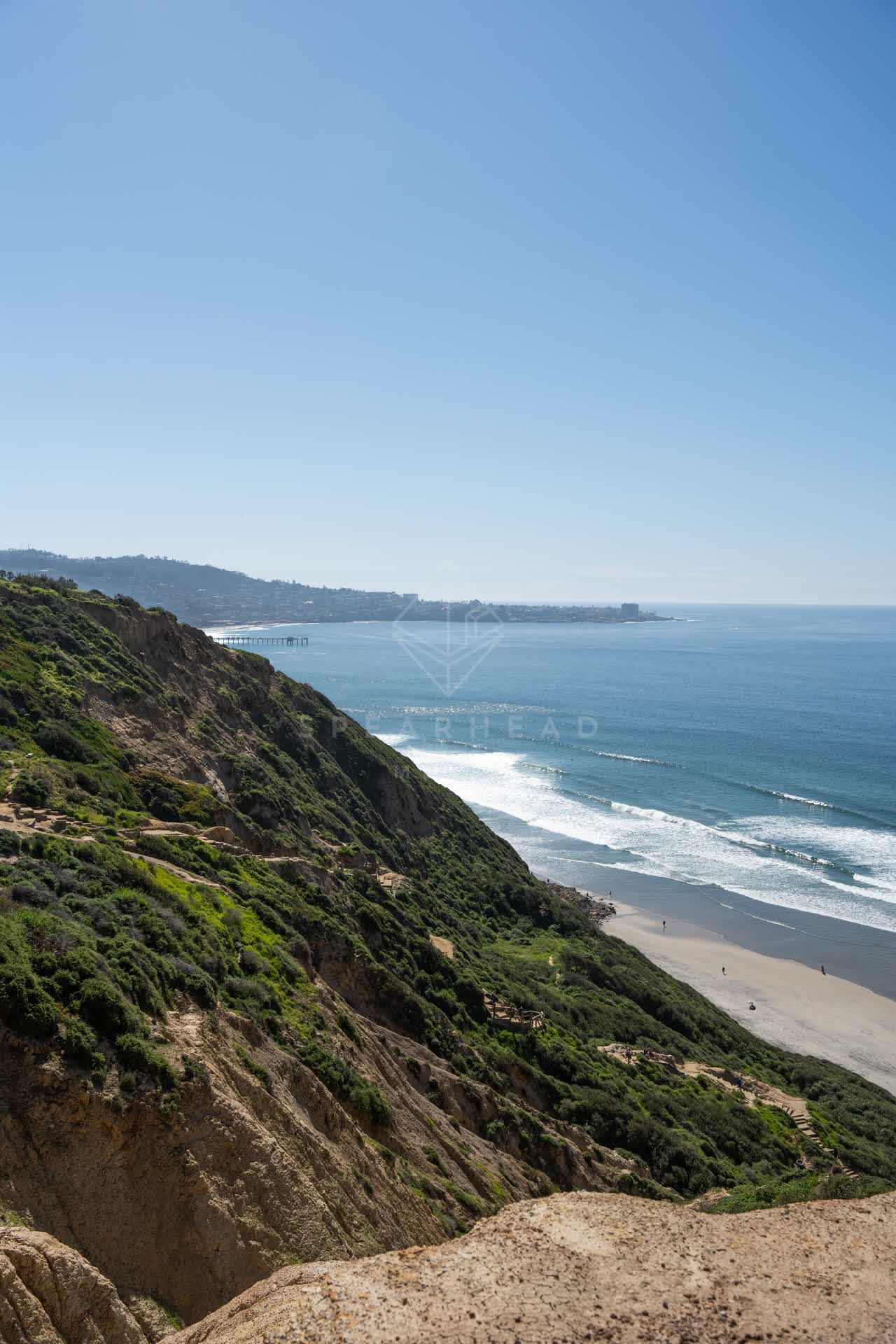 Elevated view of the cliffs, the surf and the ocean at Torrey Pines, with people walking.