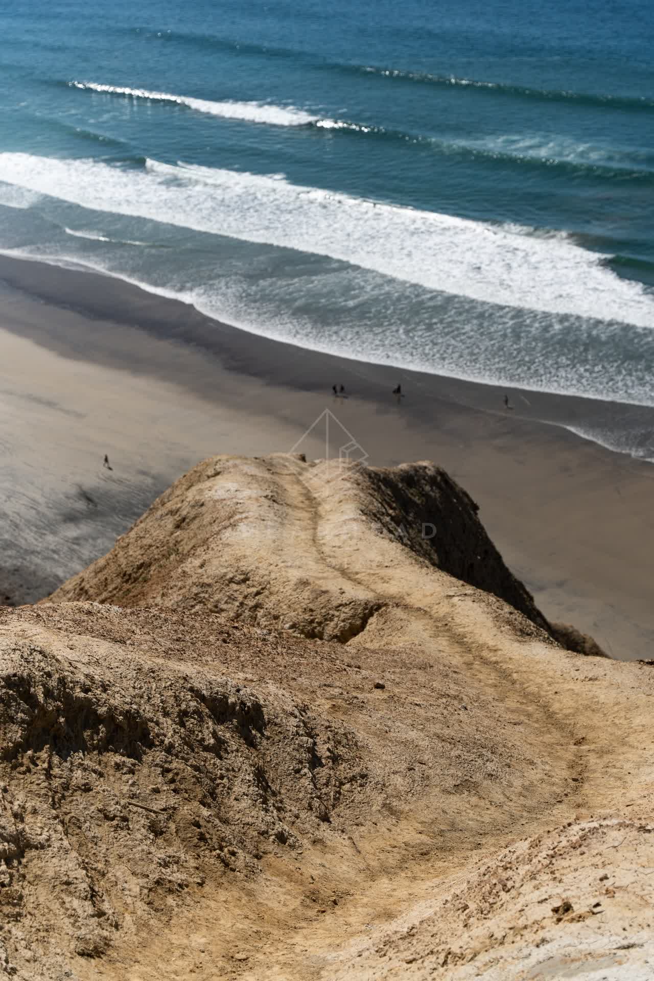Elevated view of the cliffs, the surf and the ocean at Torrey Pines, with people walking.