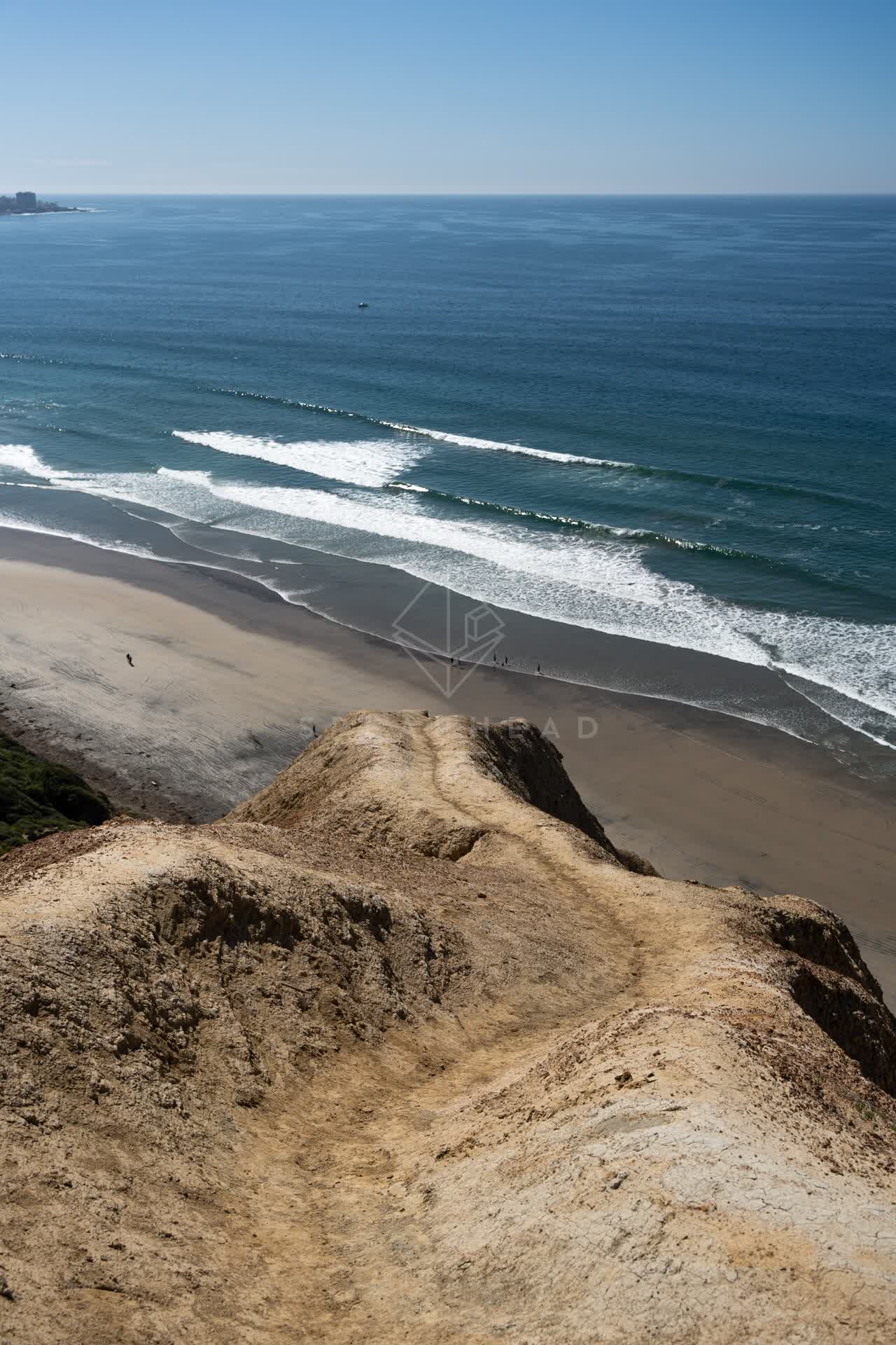 Elevated view of the cliffs, the surf and the ocean at Torrey Pines, with people walking.