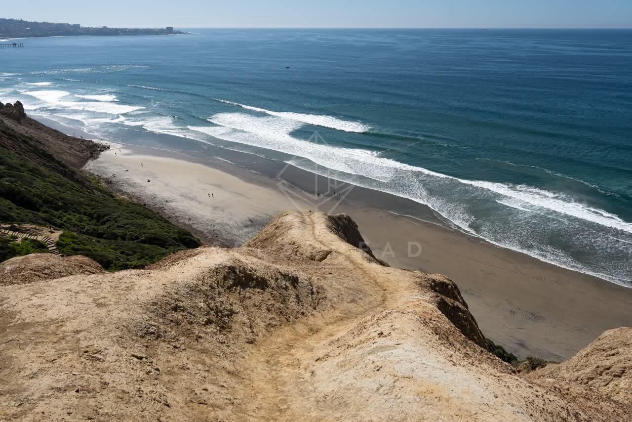 Elevated view of the cliffs, the surf and the ocean at Torrey Pines, with people walking.