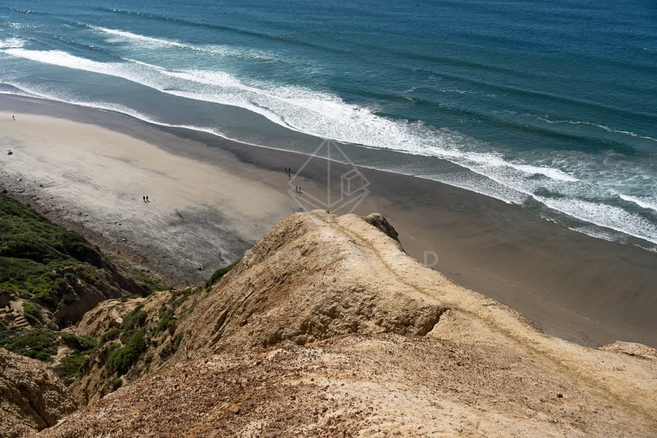 Aerial view of the cliffs, the surf and the ocean at Torrey Pines, with people walking.