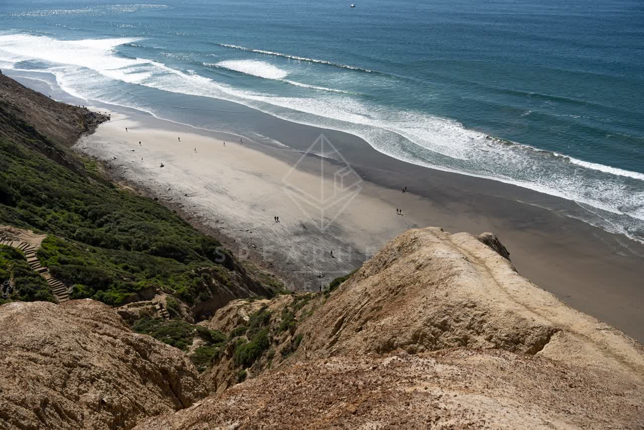 Elevated view of the cliffs, the surf and the ocean at Torrey Pines, with people walking.