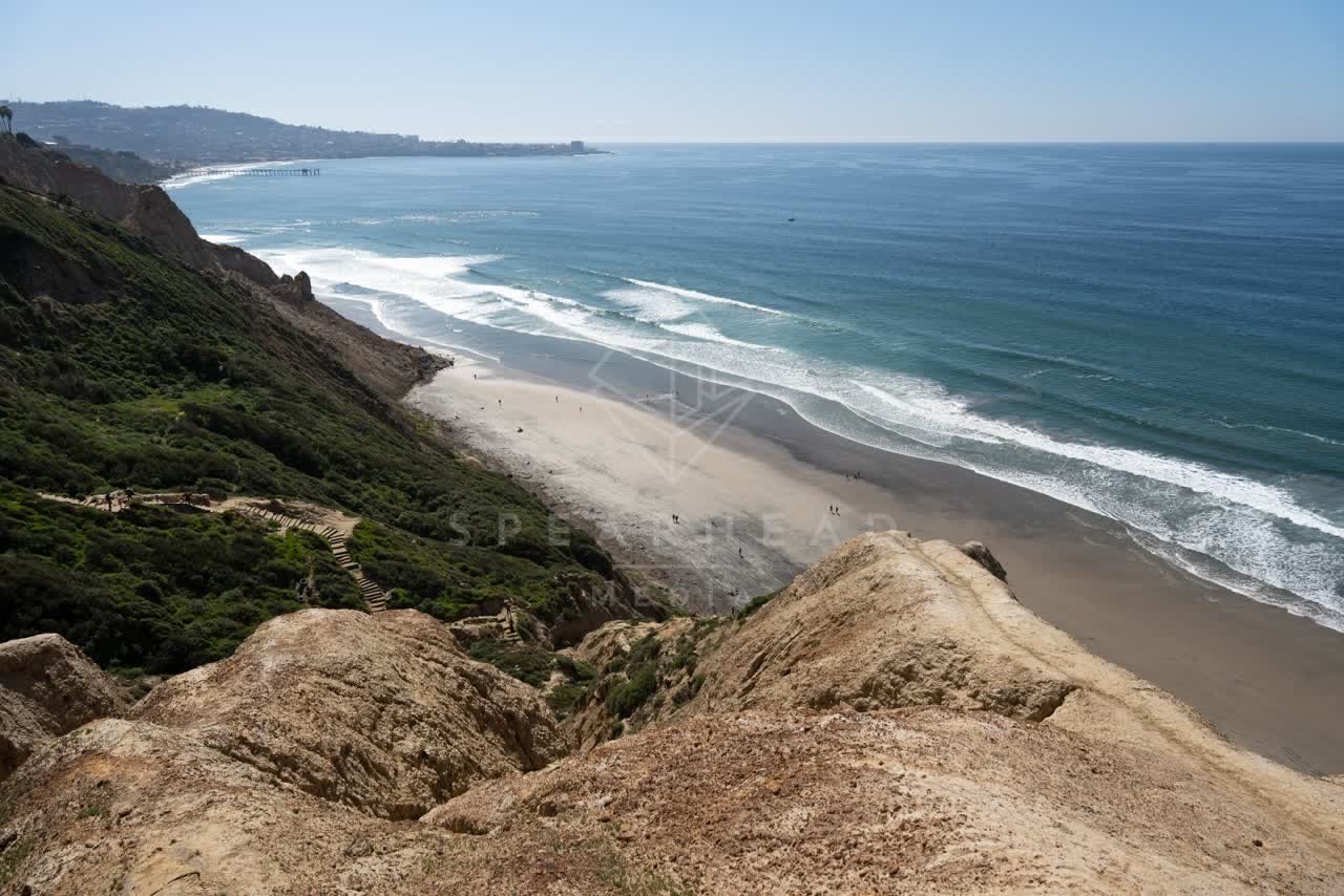Elevated view of the cliffs, the surf and the pier at Torrey Pines, with people walking.