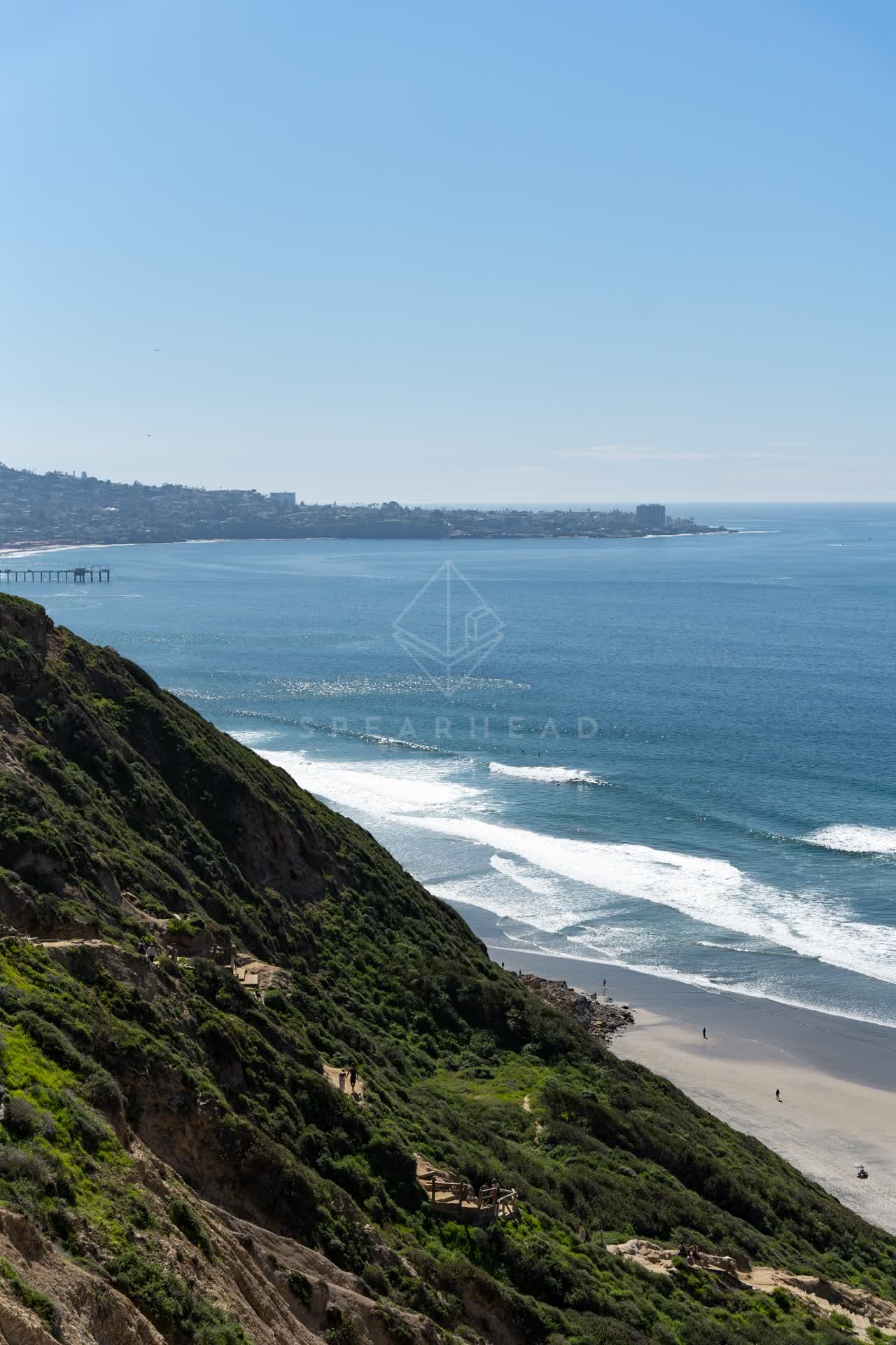 Elevated view of the cliffs, the surf and the pier at Torrey Pines, with people walking.
