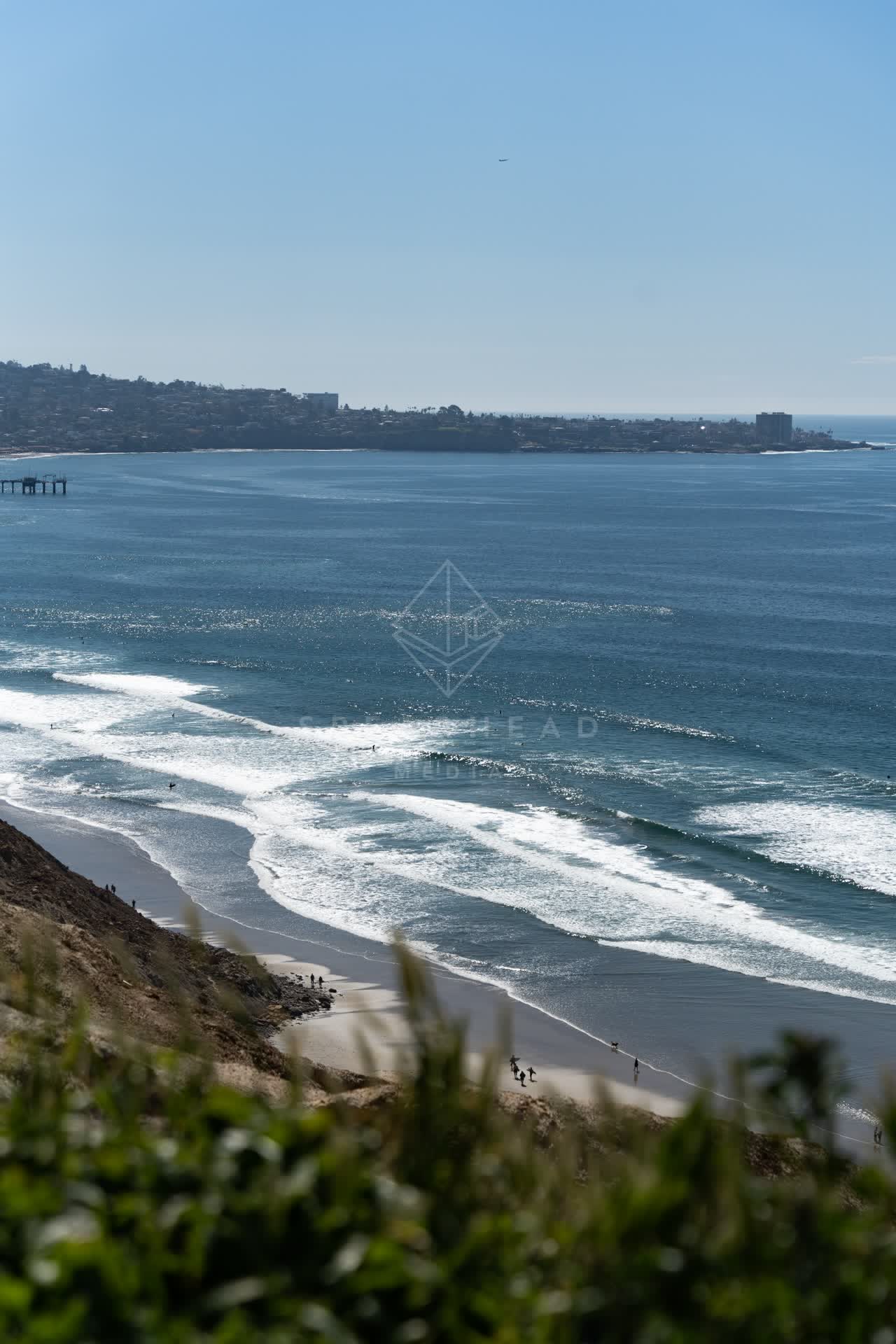 Elevated view of the cliffs, the surf and the ocean at Torrey Pines, with people walking.