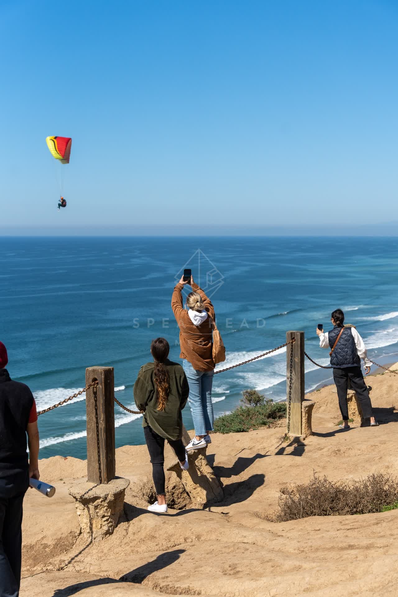 Elevated view of the cliffs, the ocean and the beach at Torrey Pines, with a crowd gathered.