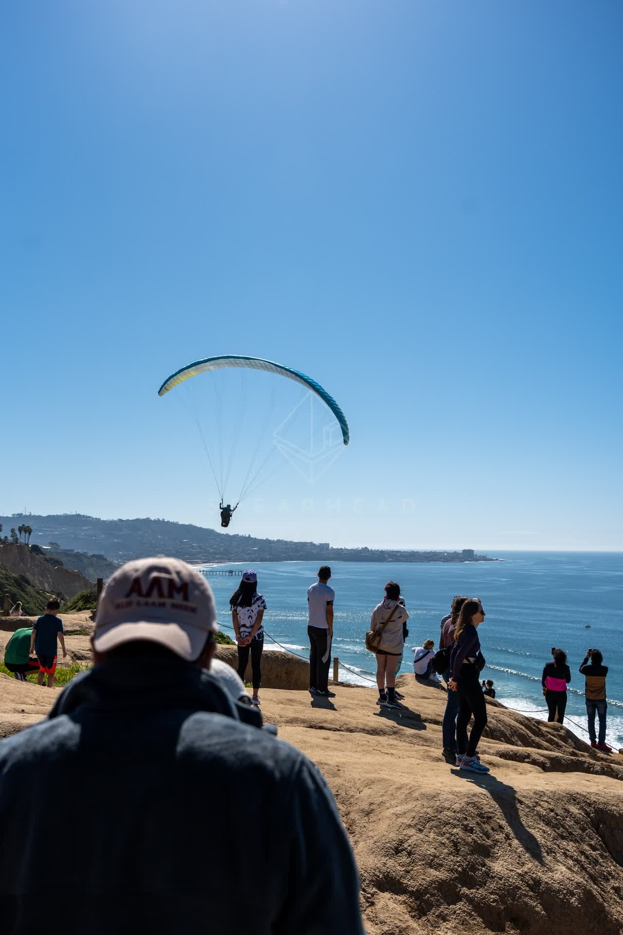 Elevated view of the cliffs, the pier and the ocean at Torrey Pines, with a crowd gathered.