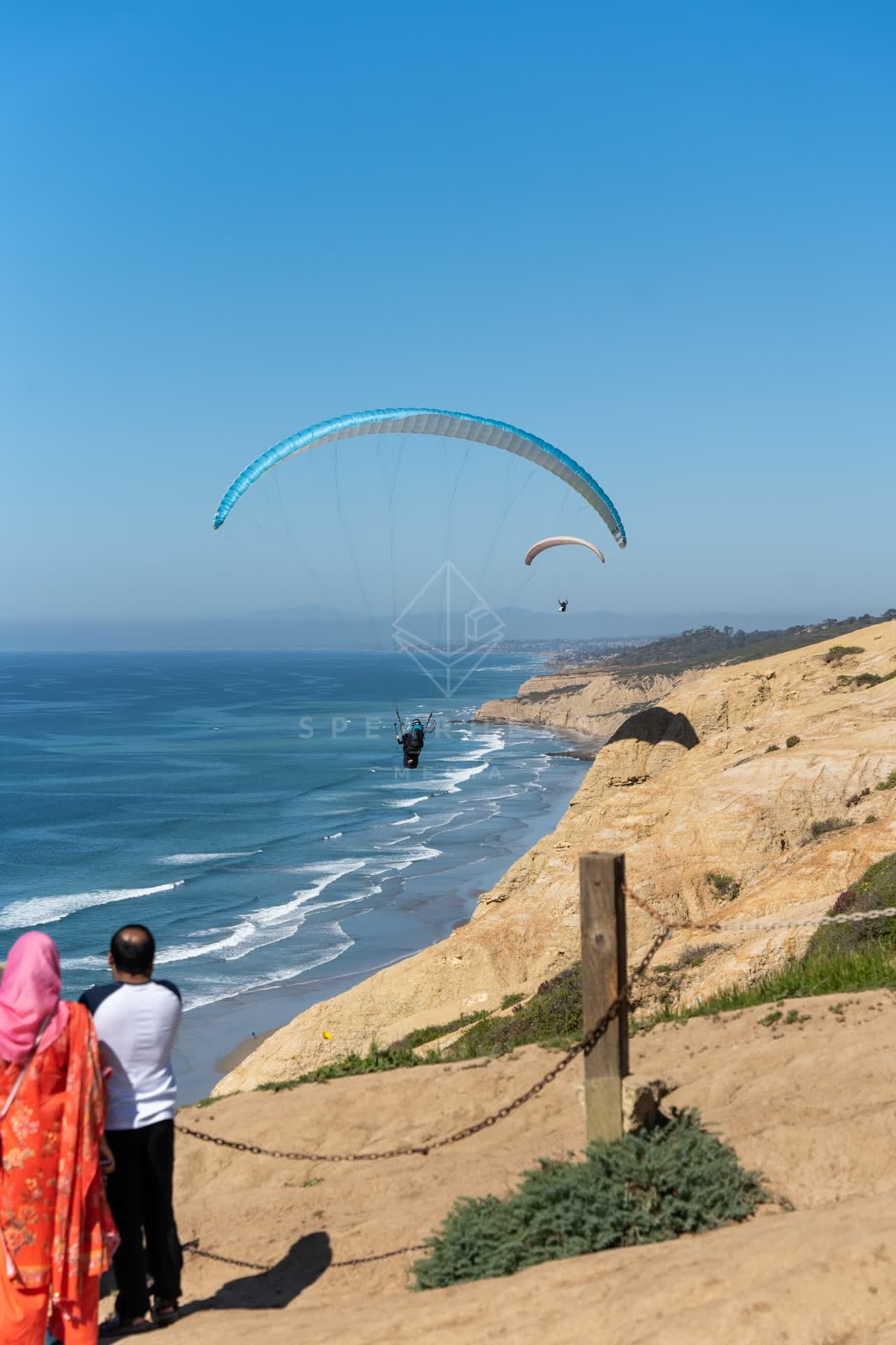 Elevated view of the cliffs, the ocean and the beach at Torrey Pines, with a crowd gathered.
