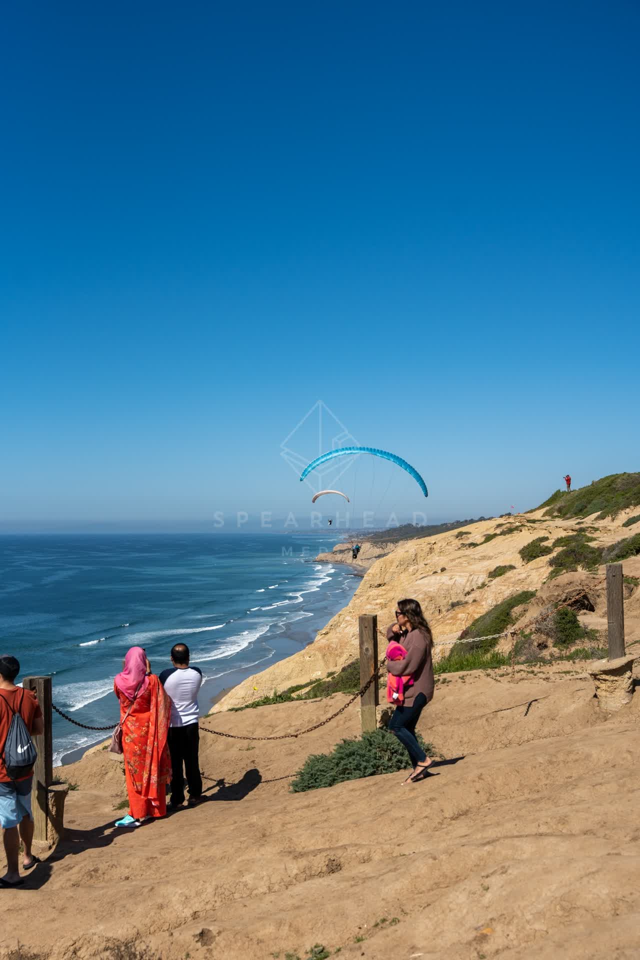 Elevated view of the cliffs, the ocean and the beach at Torrey Pines, with a crowd gathered.