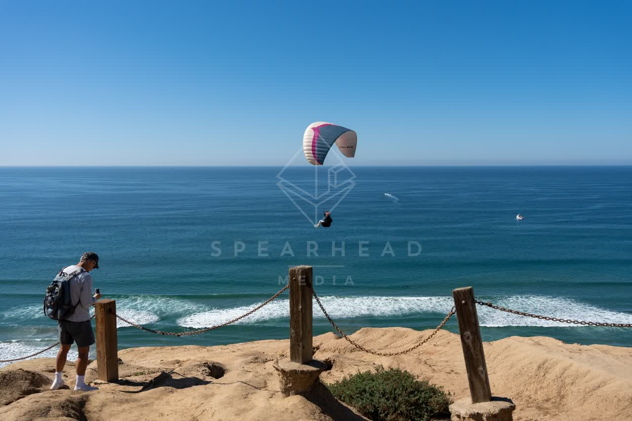 Elevated view of the cliffs, the surf and boats at Torrey Pines, with a crowd gathered.