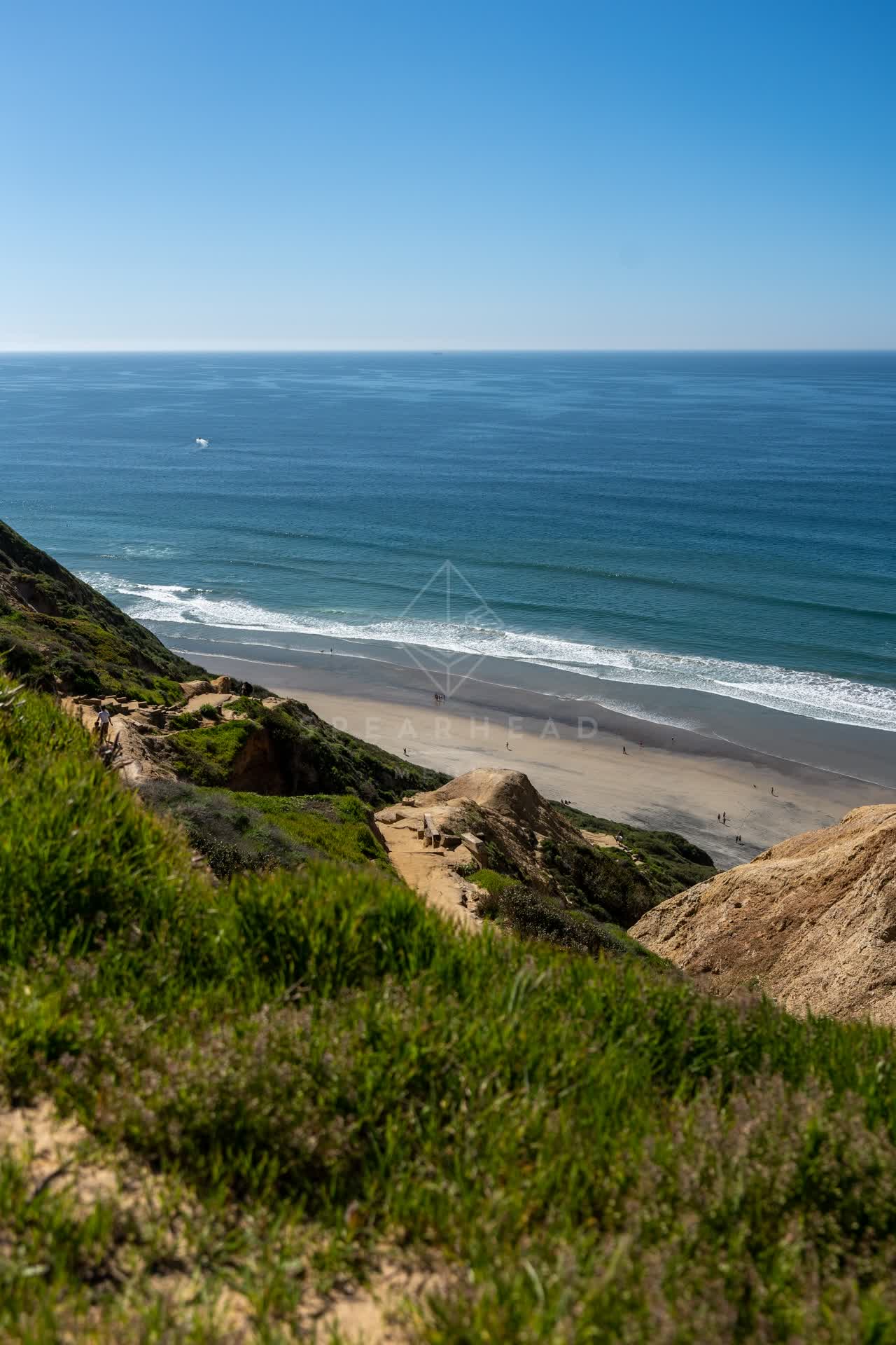Elevated view of the cliffs, the surf and the ocean at Torrey Pines, with people walking.
