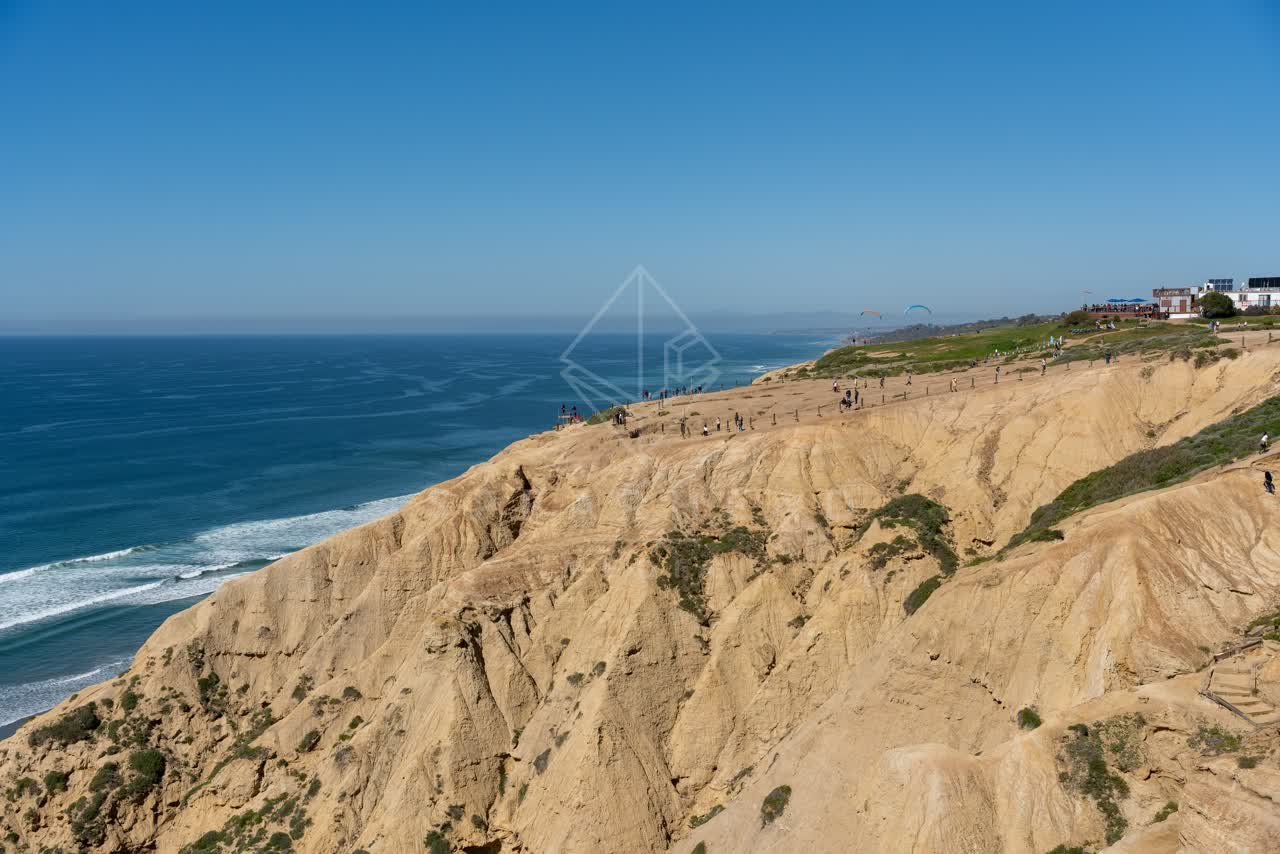 Elevated view of the cliffs, the surf and the ocean at Torrey Pines, with people walking.
