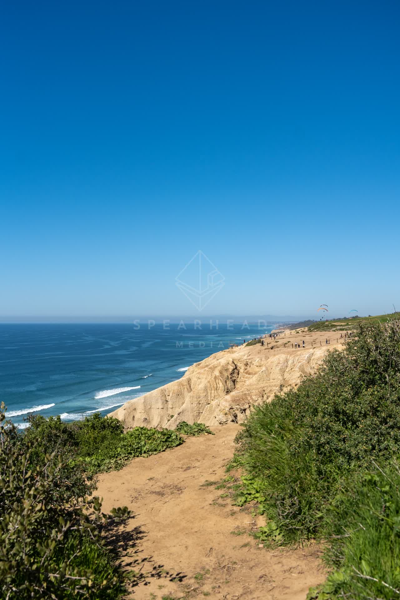 Elevated view of the cliffs, the surf and the ocean at Torrey Pines, with people walking.