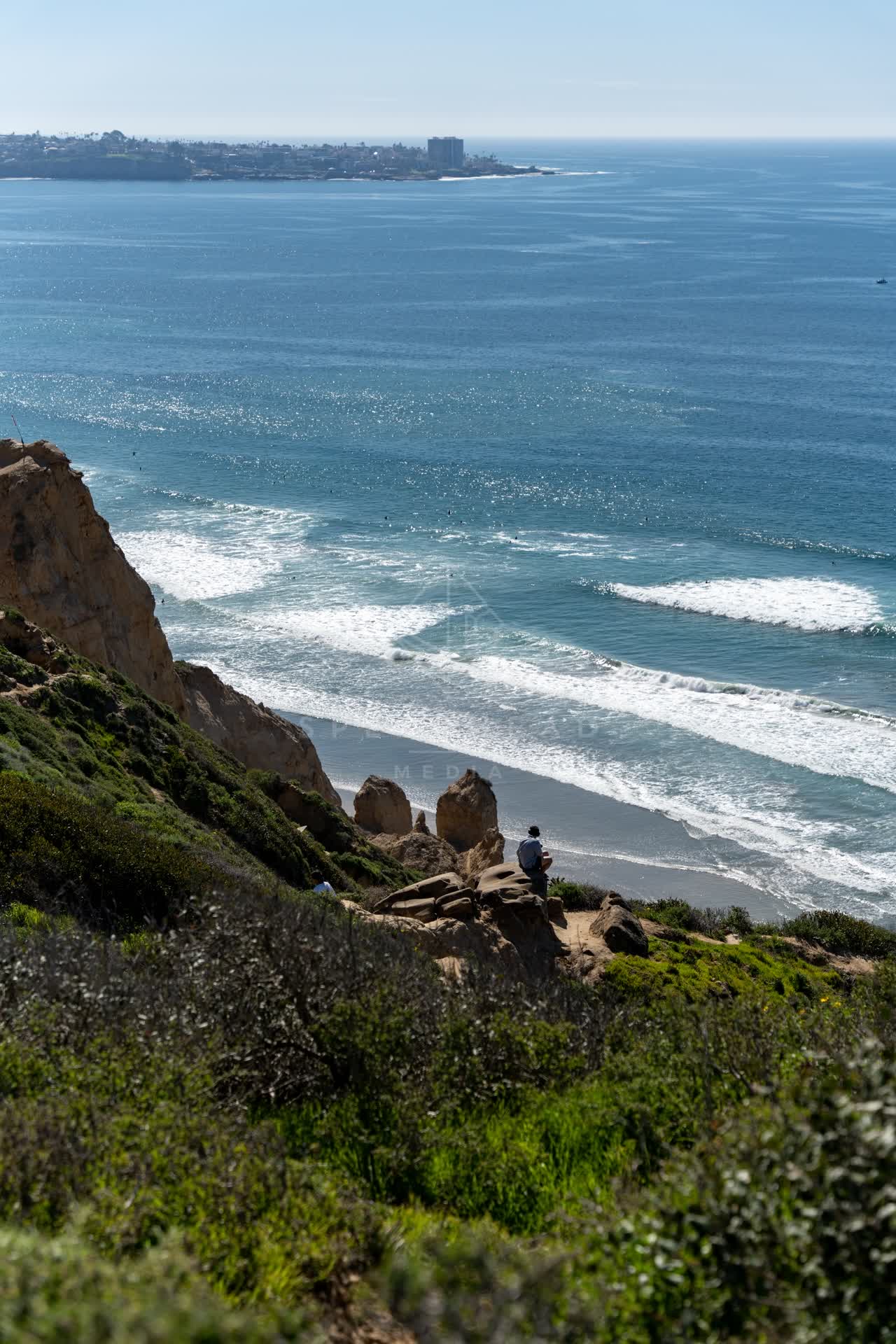 Elevated view of the cliffs, the surf and the ocean at Torrey Pines, with people walking.