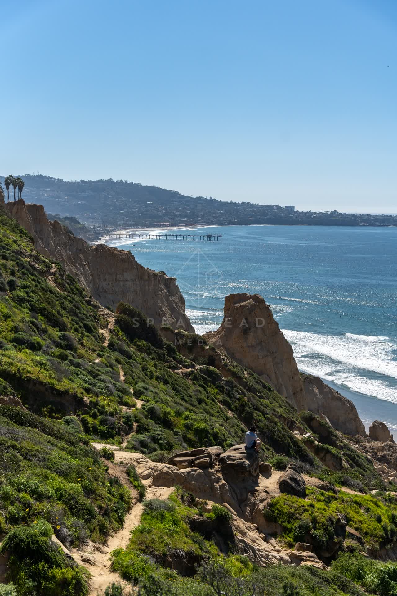 Elevated view of the cliffs, the surf and the pier at Torrey Pines, with people walking.