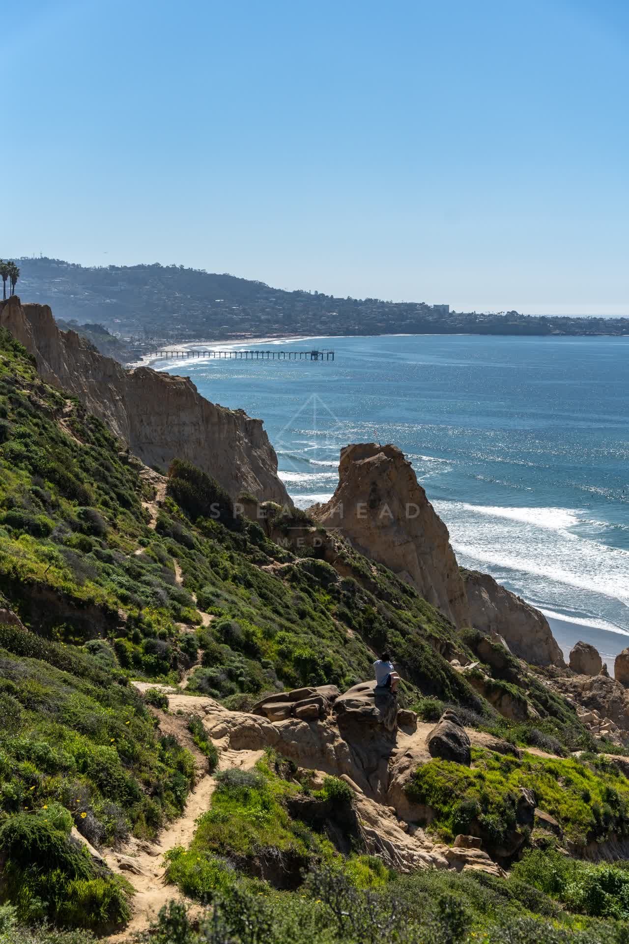 Elevated view of the cliffs, the surf and the pier at Torrey Pines, with people walking.