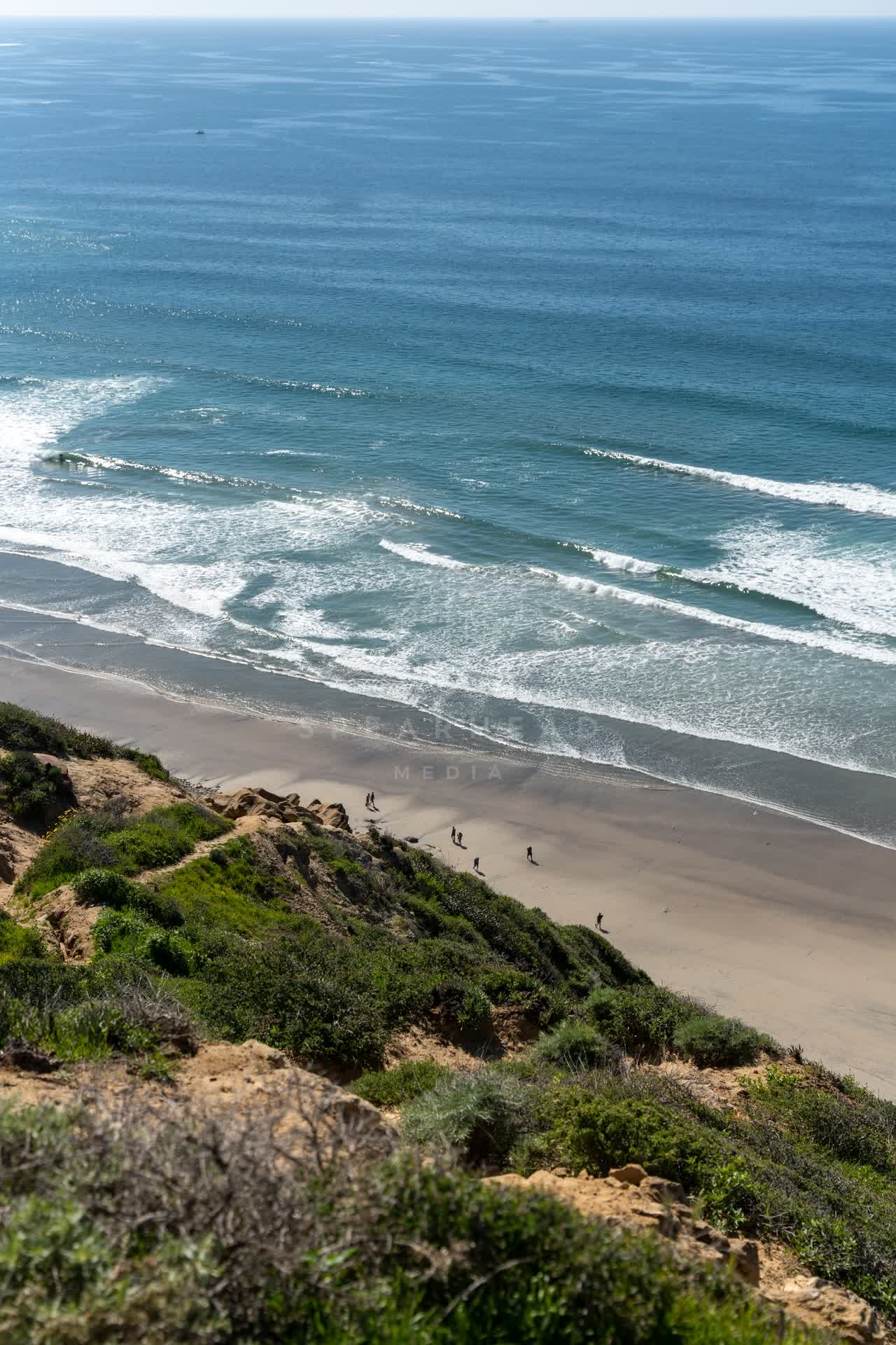 Elevated view of the cliffs, the surf and the ocean at Torrey Pines, with people walking.
