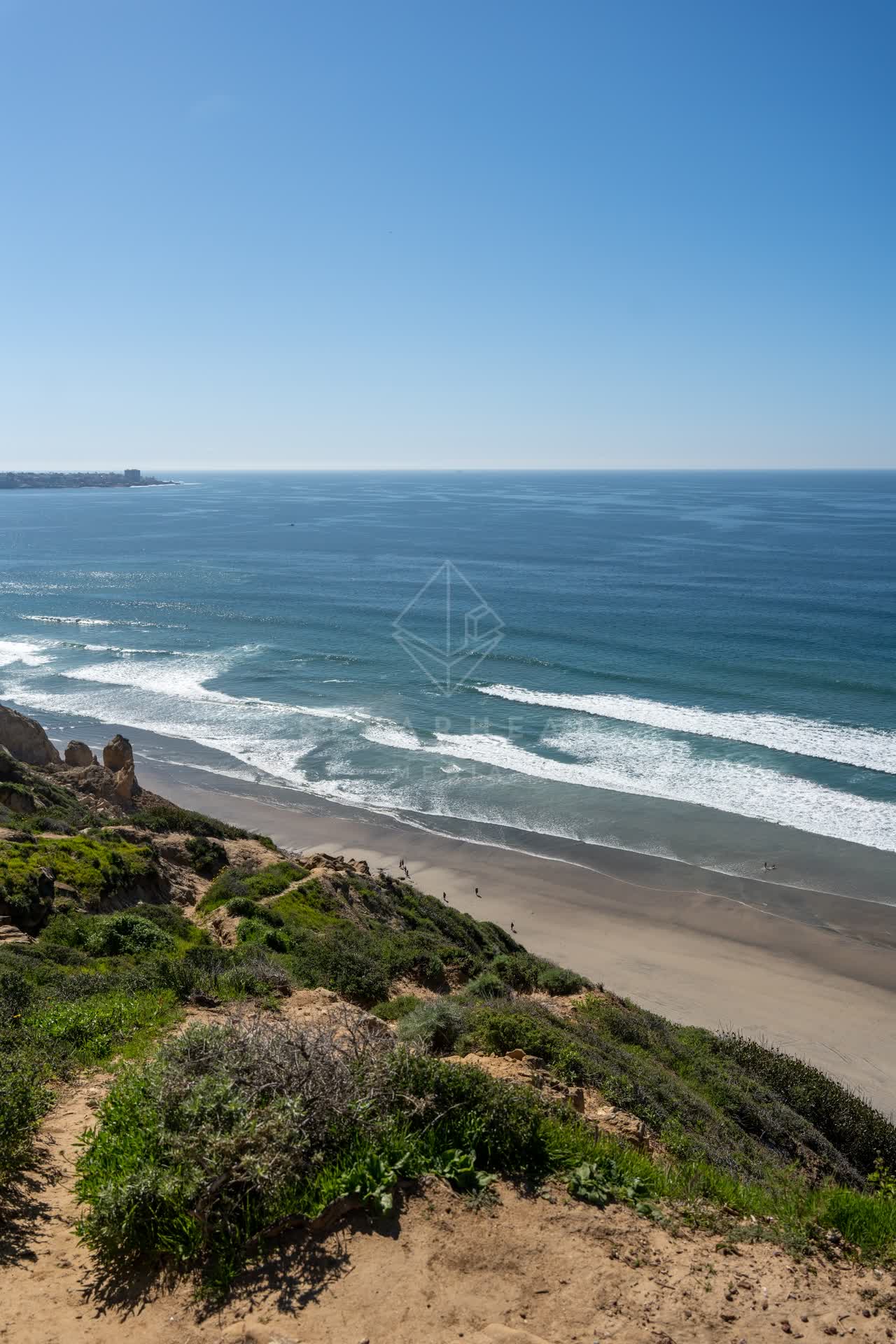 Elevated view of the cliffs, the surf and the ocean at Torrey Pines, with people walking.