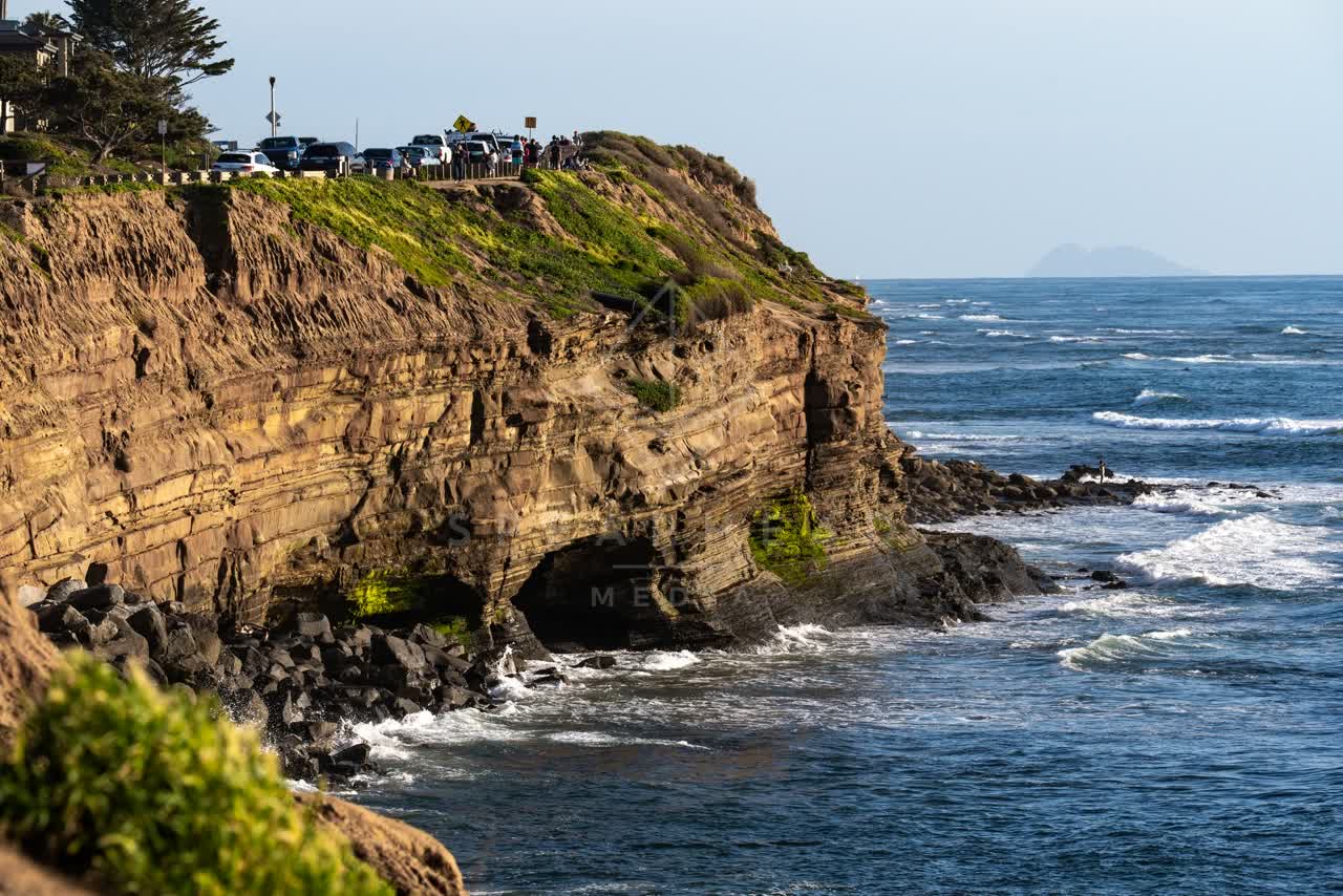 Elevated view of the cliffs, the ocean and traffic at Sunset Cliffs, with people walking.