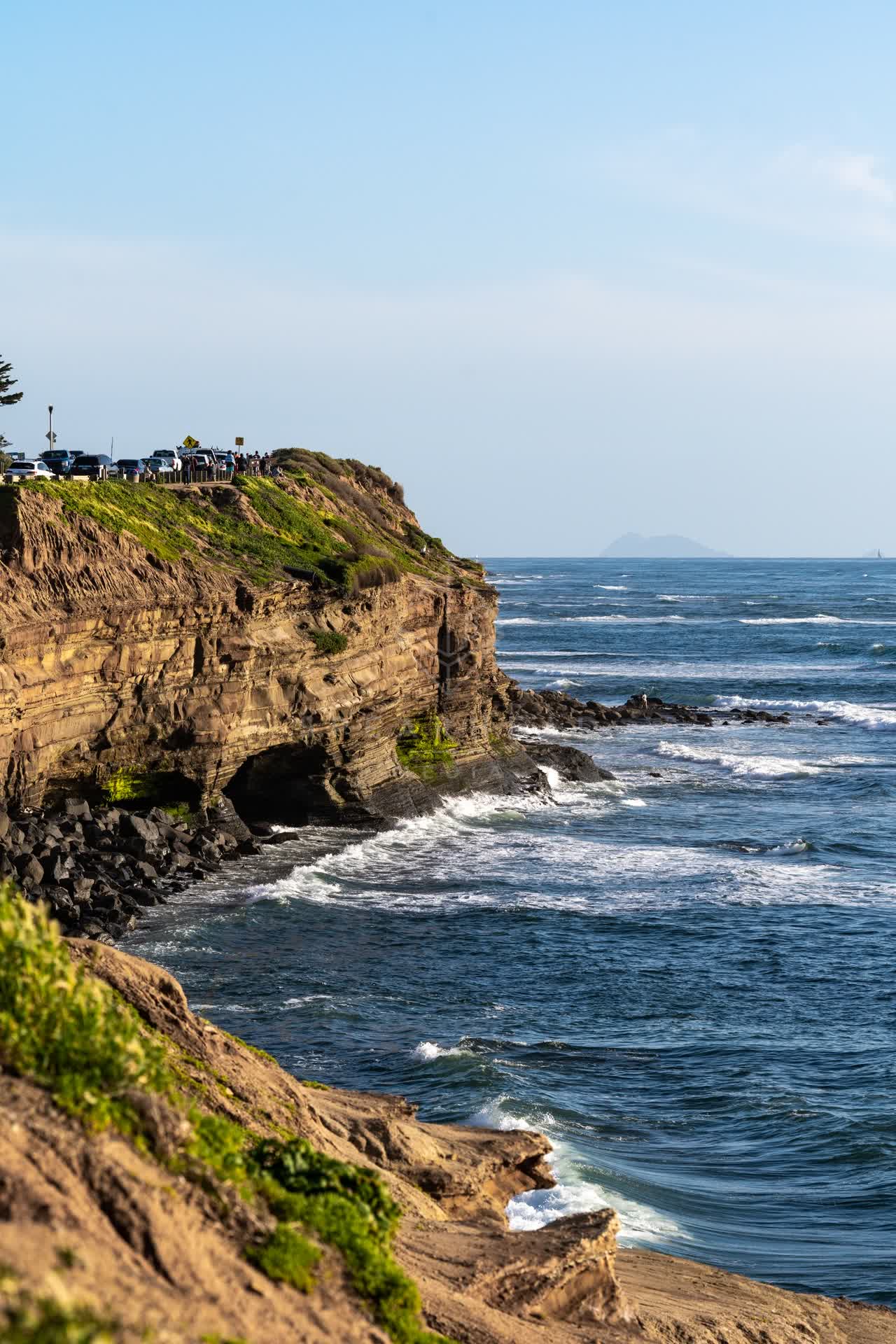 Elevated view of the cliffs, the surf and the ocean at Sunset Cliffs, with people walking.